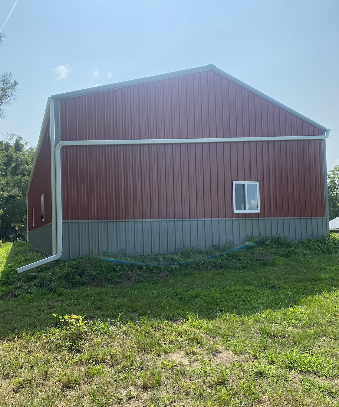 Red barn with a small window, white trim, green grass in front, and a blue sky with some clouds