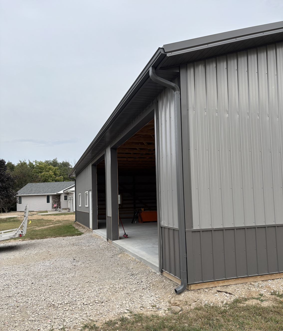 Exterior view of a partially constructed metal building with a open garage door, metal siding, and a gravel driveway in front.