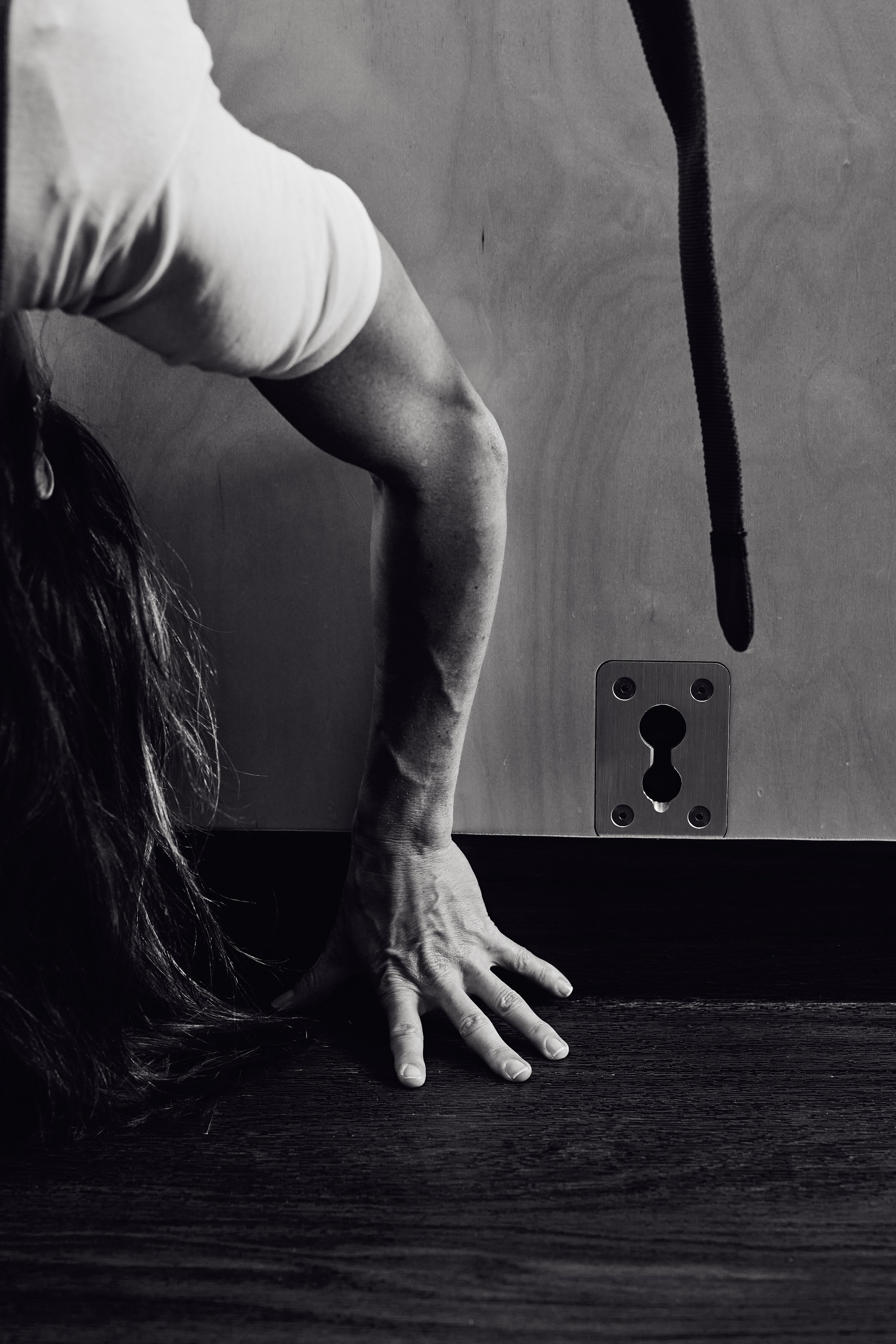 Backbend with one hand pressed to the studio floor beside the wall ropes