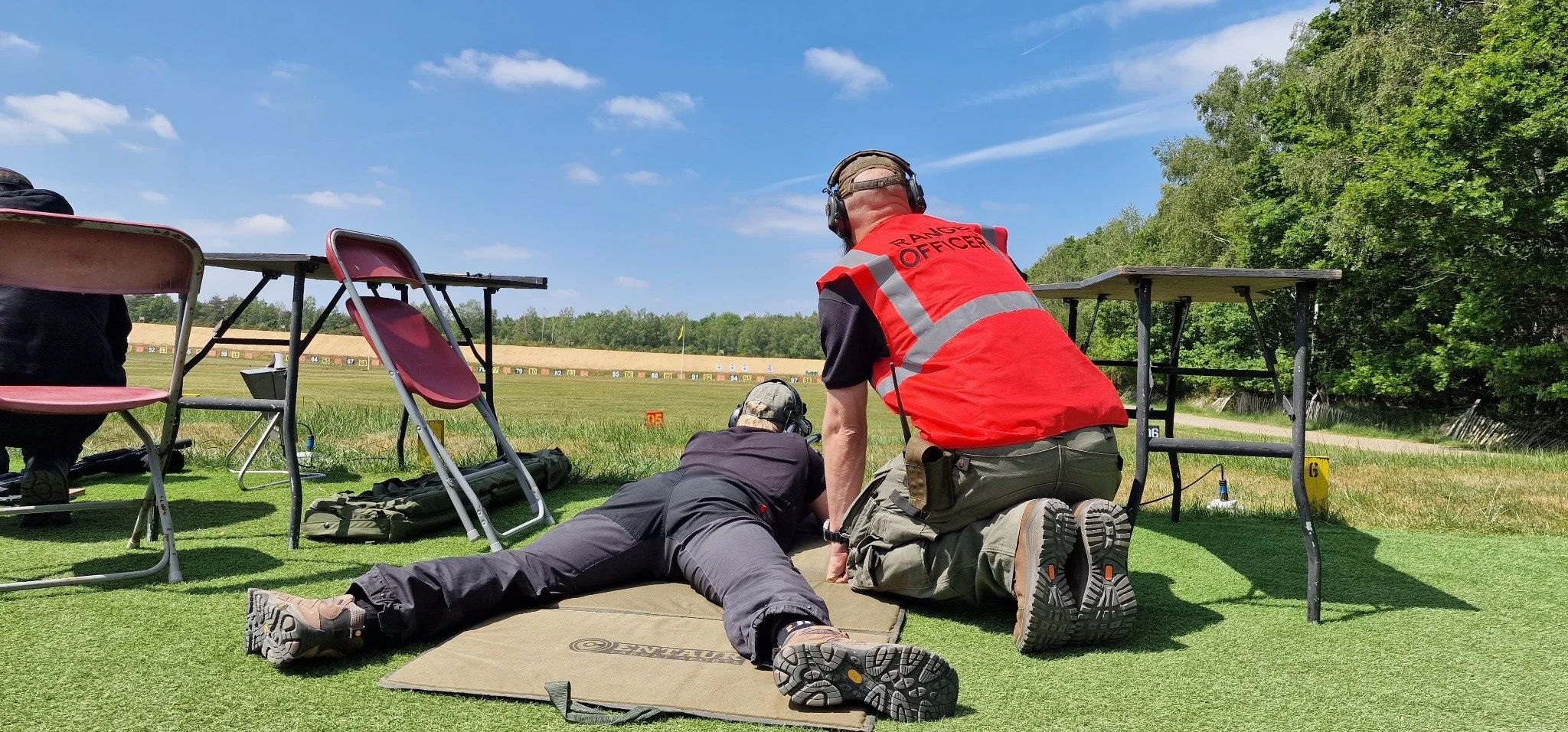 Range officer coaching a prone rifle shooter at an outdoor range