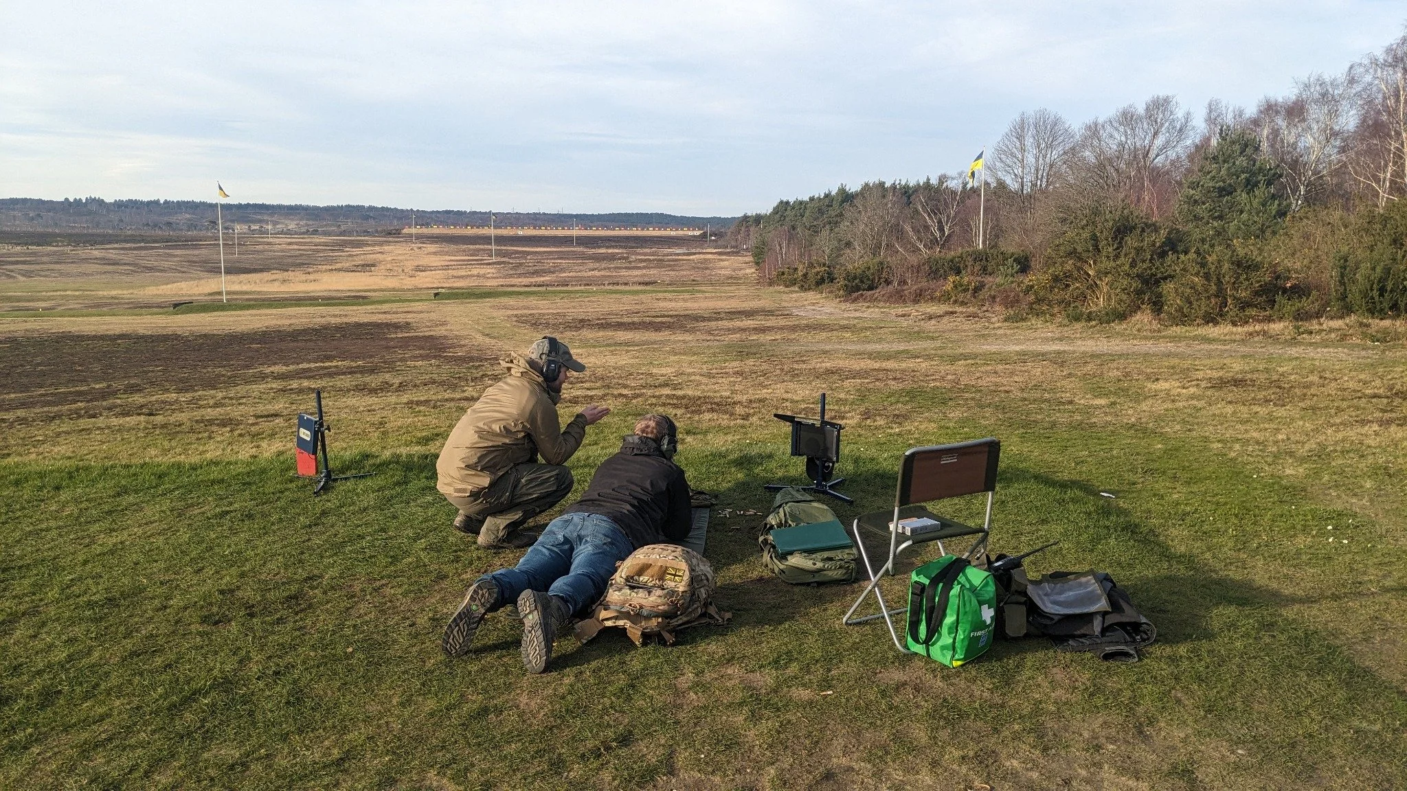 Two people at an outdoor rifle range, one coaching a prone shooter