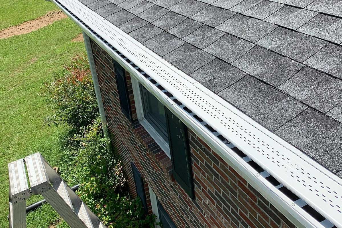 View of a house with a brick exterior, gray shingle roof, and LeafX gutter protection.