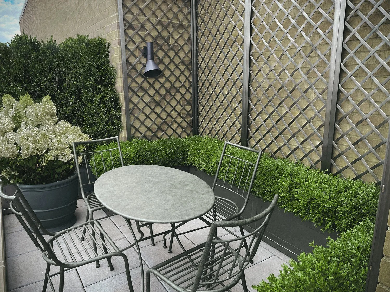 Round table and chairs beside a blackened steel trellis and clipped boxwood, Park Avenue Penthouse