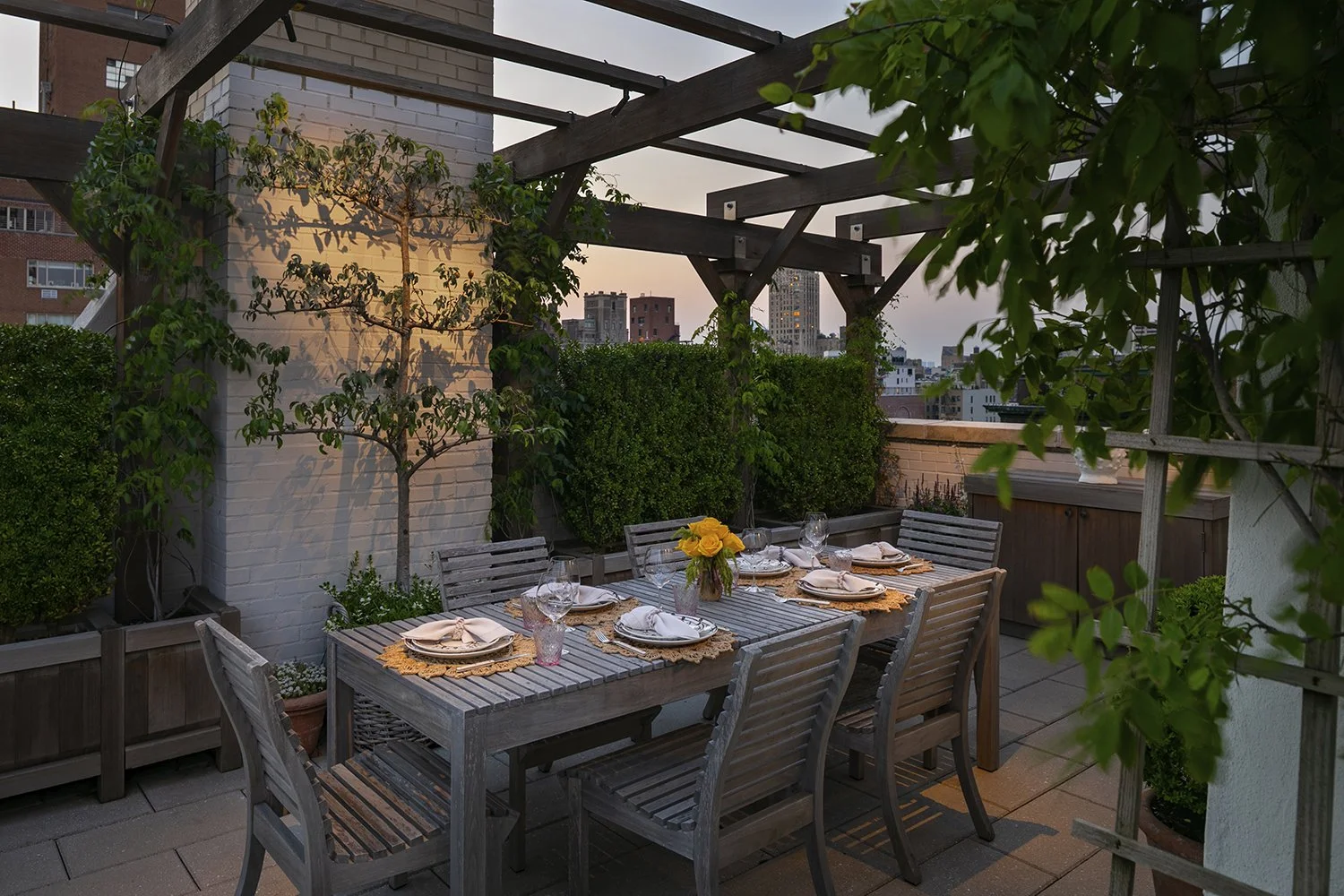 Rooftop dining terrace beneath a planted pergola at dusk, In the City, David Eaton Associates