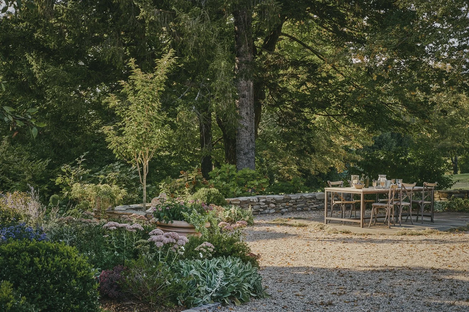Dining table in the gravel garden beneath mature trees, Hudson Valley Estate, Rhinebeck
