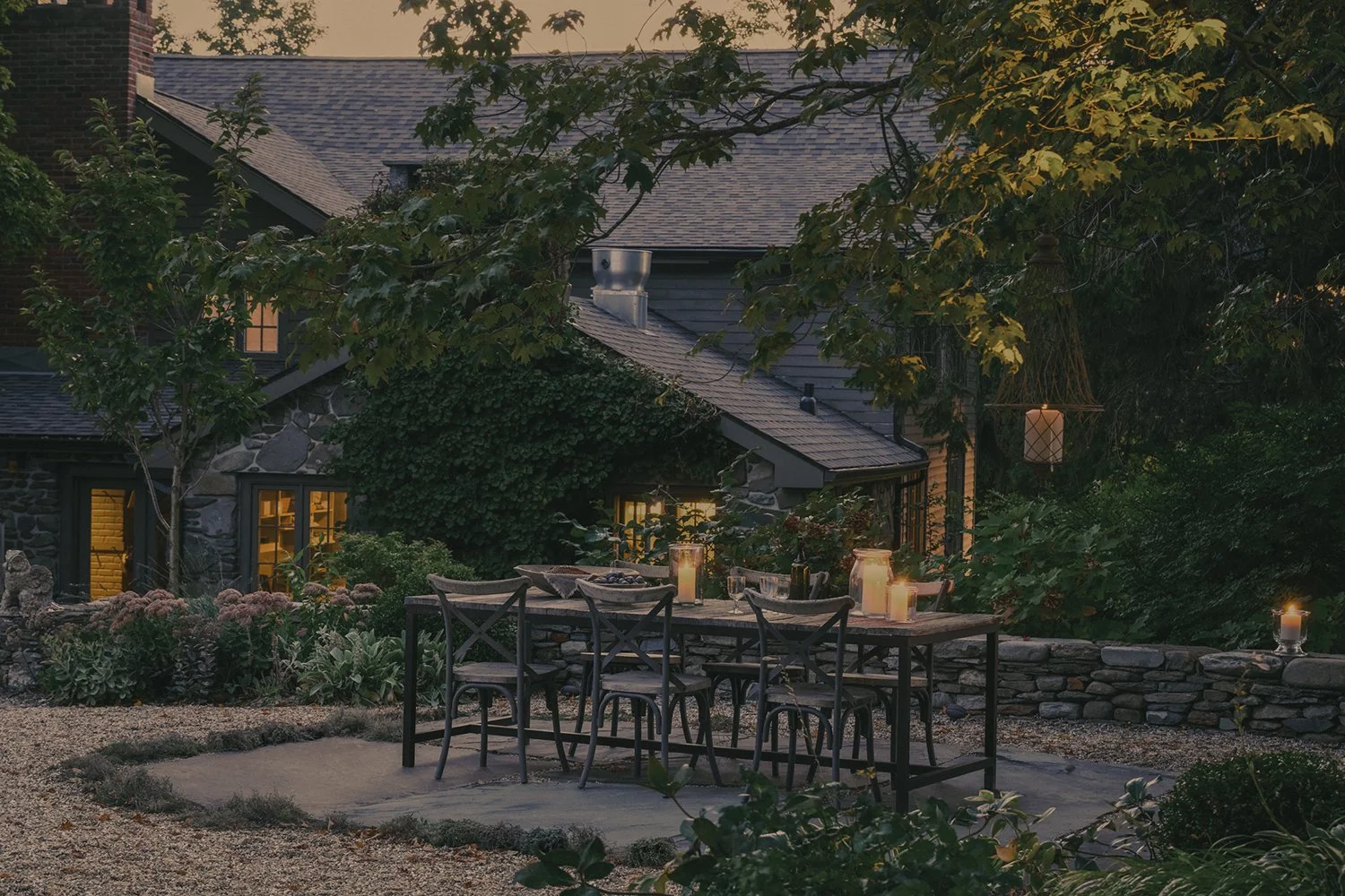 Dining terrace at dusk beside the lit house, Hudson Valley Estate, Rhinebeck