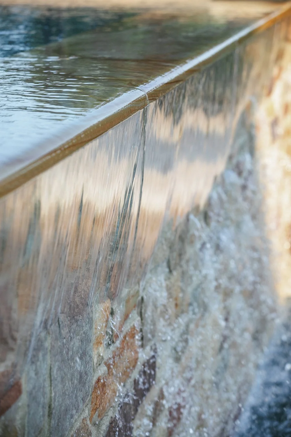 Water spilling over the pool's negative edge against layered stone, Riverfront Estate, Navesink River