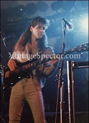 Musician playing bass guitar on stage with microphone stand nearby at a concert.