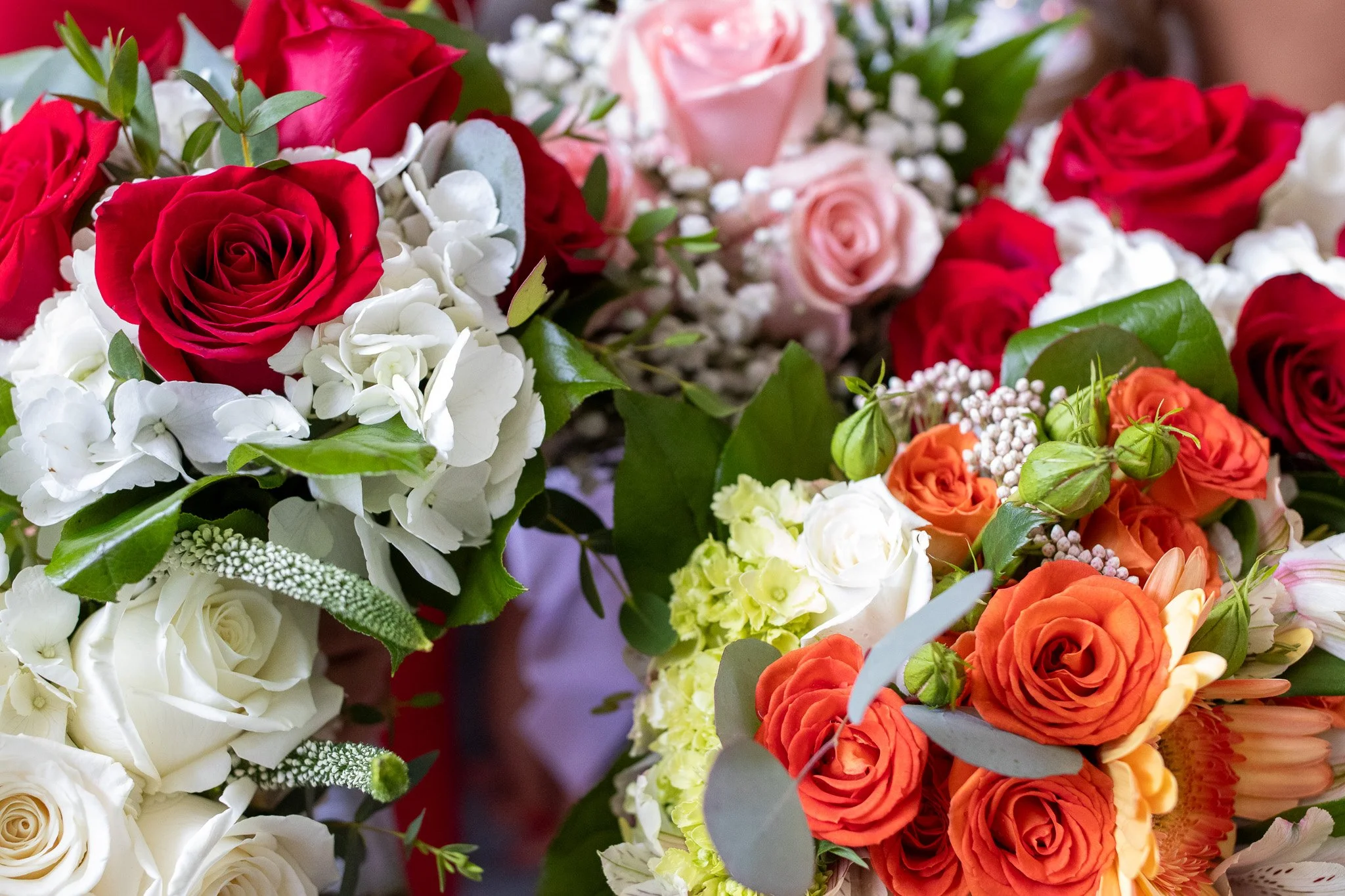 Close-up of colorful bouquet of roses and other flowers in shades of red, pink, orange, white, with green leaves.
