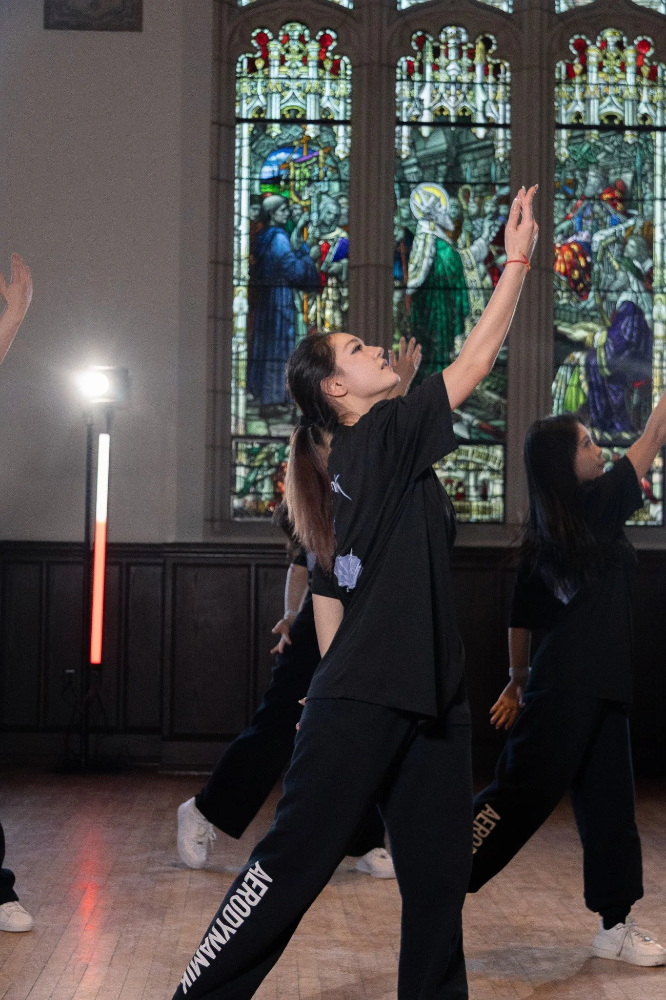 Group of people dancing inside a church with stained glass windows in the background.