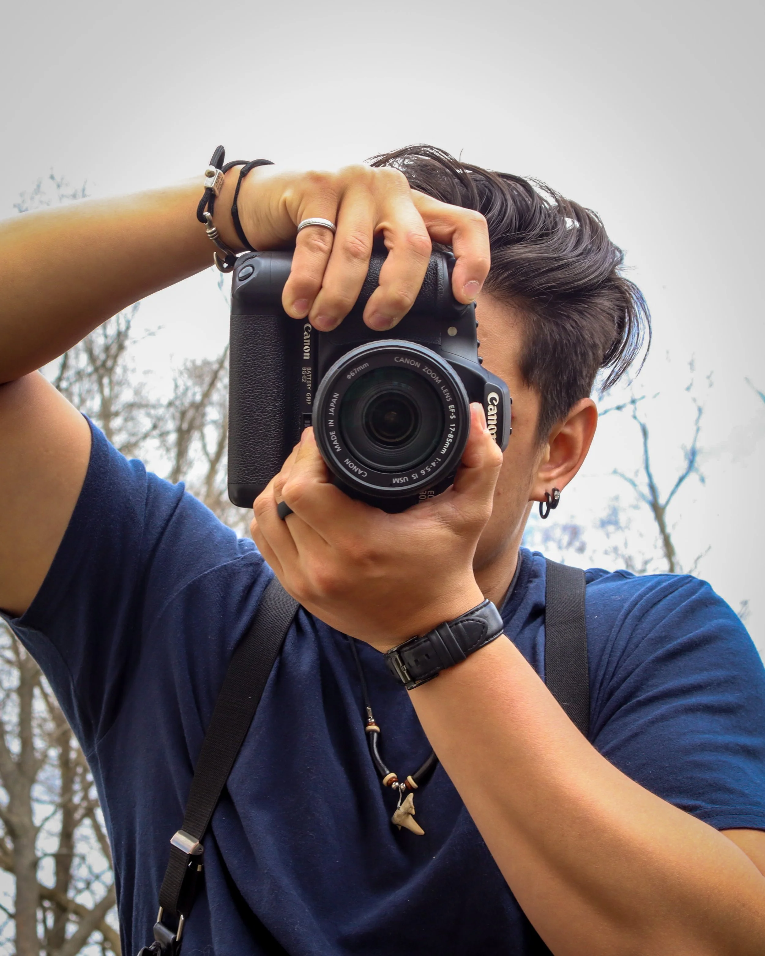 A person holding a Canon camera to their face, taking a self-portrait outdoors, with trees in the background.