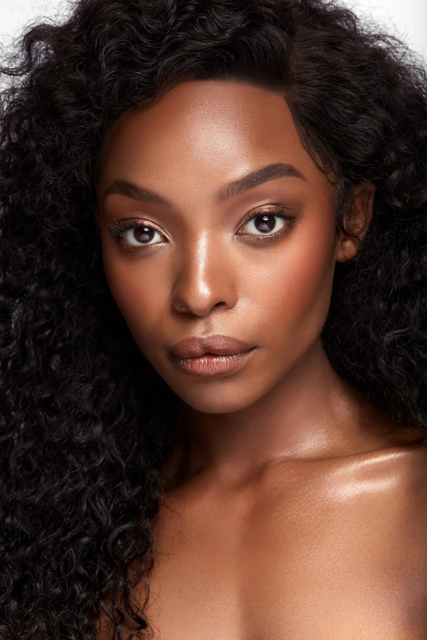 Close-up of a woman with dark curly hair, smooth skin, and makeup on her eyes and lips.