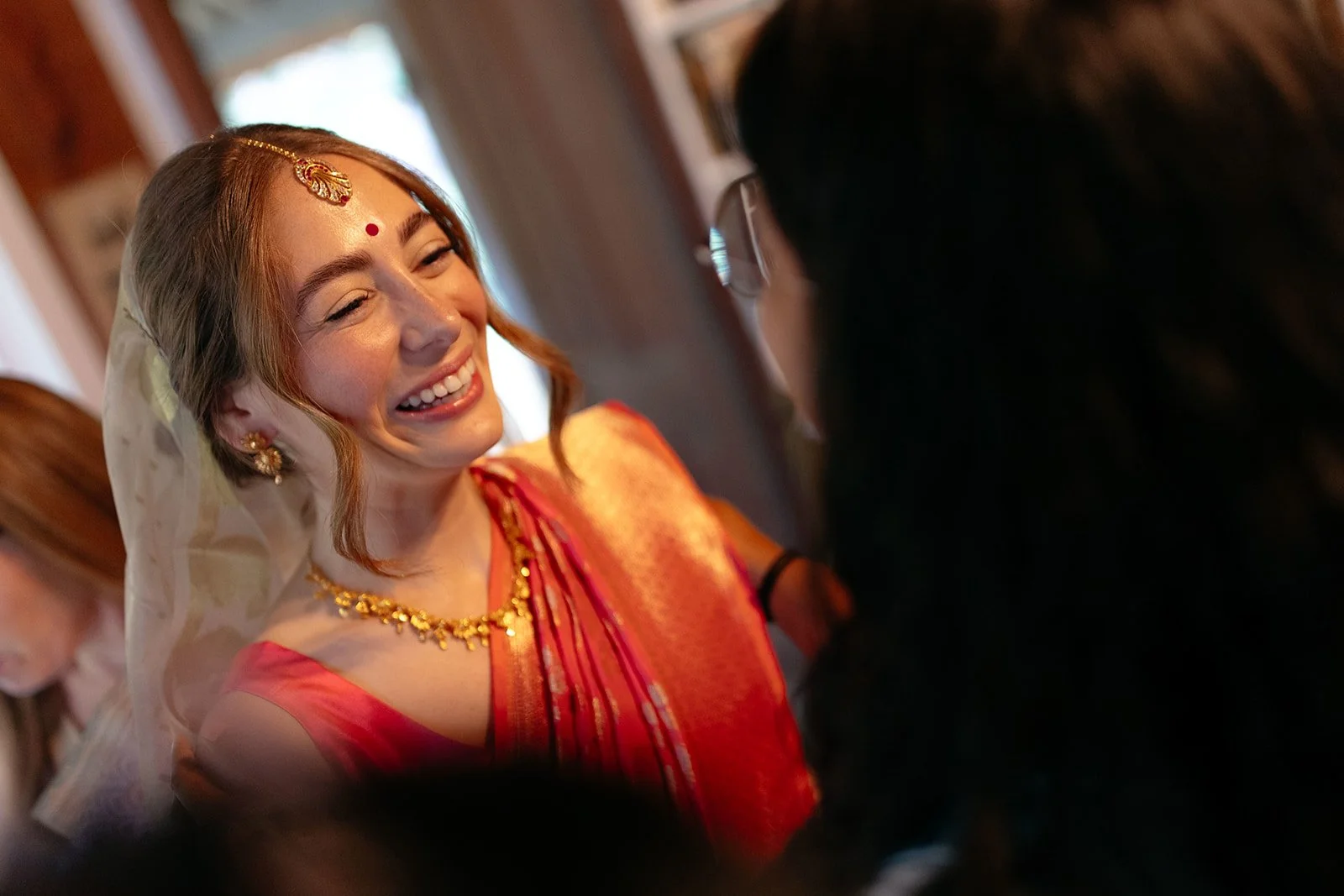 A woman dressed in traditional South Asian attire, smiling and looking at another person, during a celebration or special occasion.
