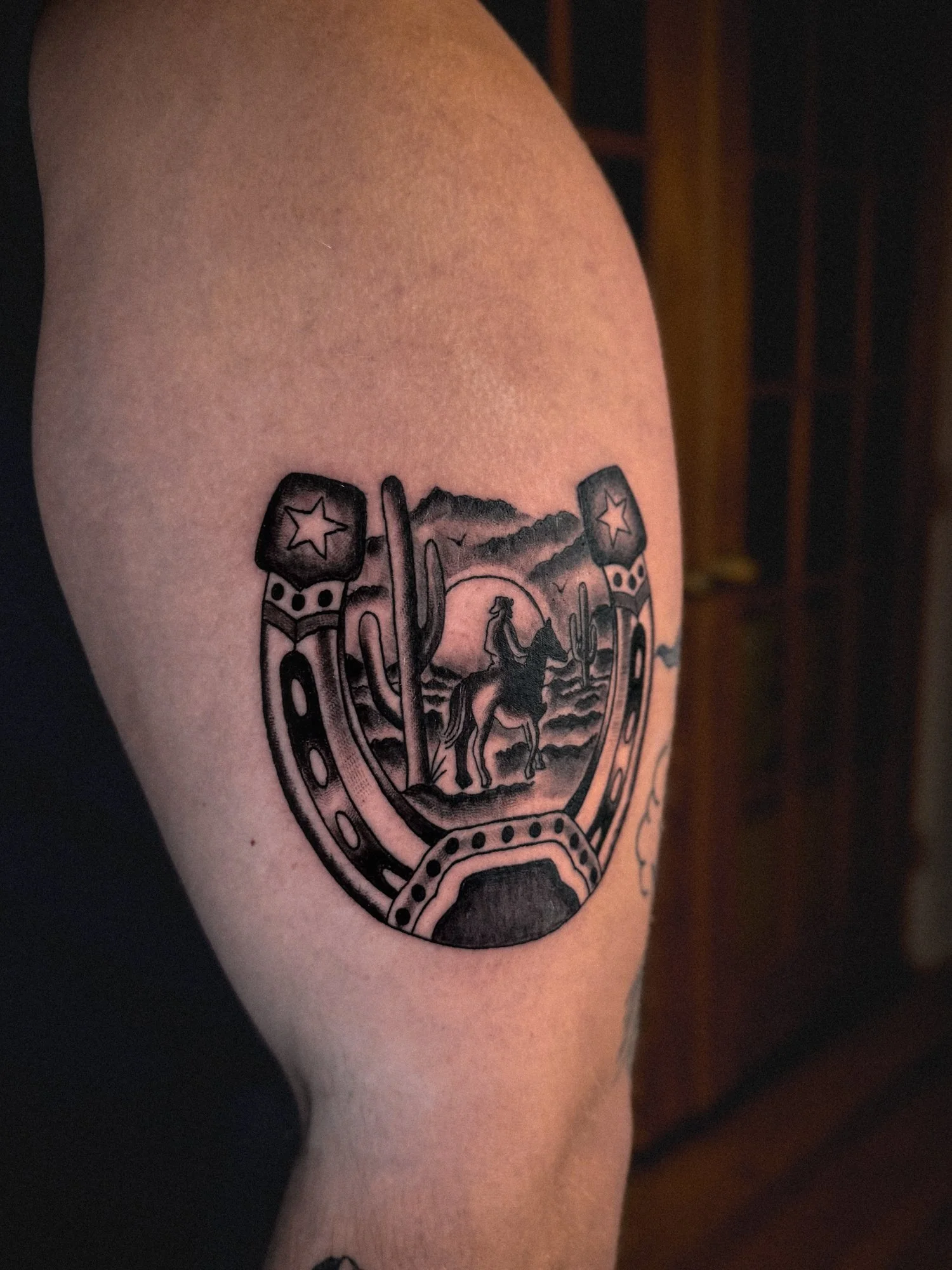 Traditional horseshoe tattoo with a desert scene of a cowboy riding into the sunset on the outer bicep.