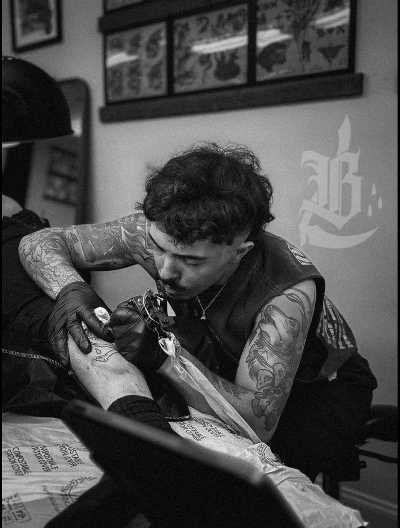 A person with tattoos on their arms, wearing gloves, getting a tattoo on their arm in a tattoo studio.