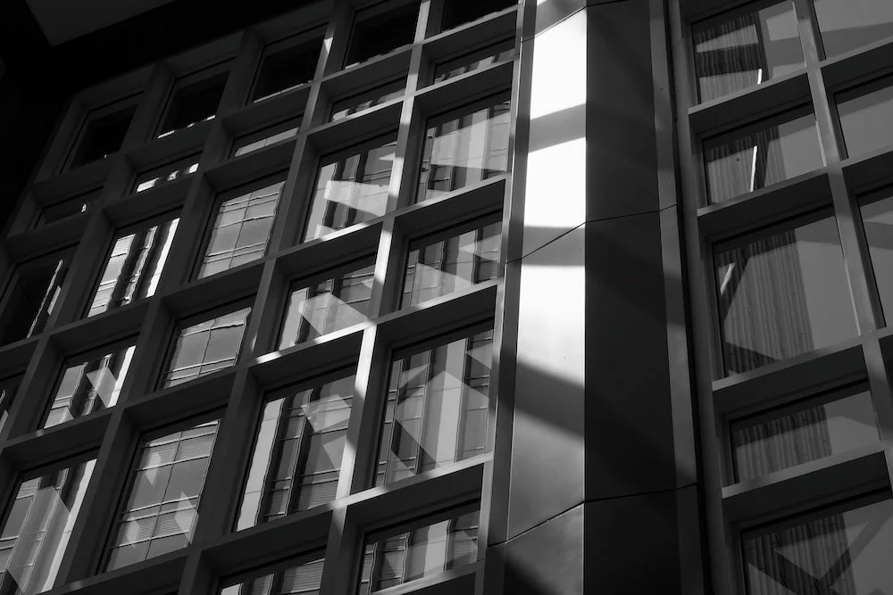 Close-up view of modern glass building facade with grid-like windows reflecting sky and clouds, black and white
