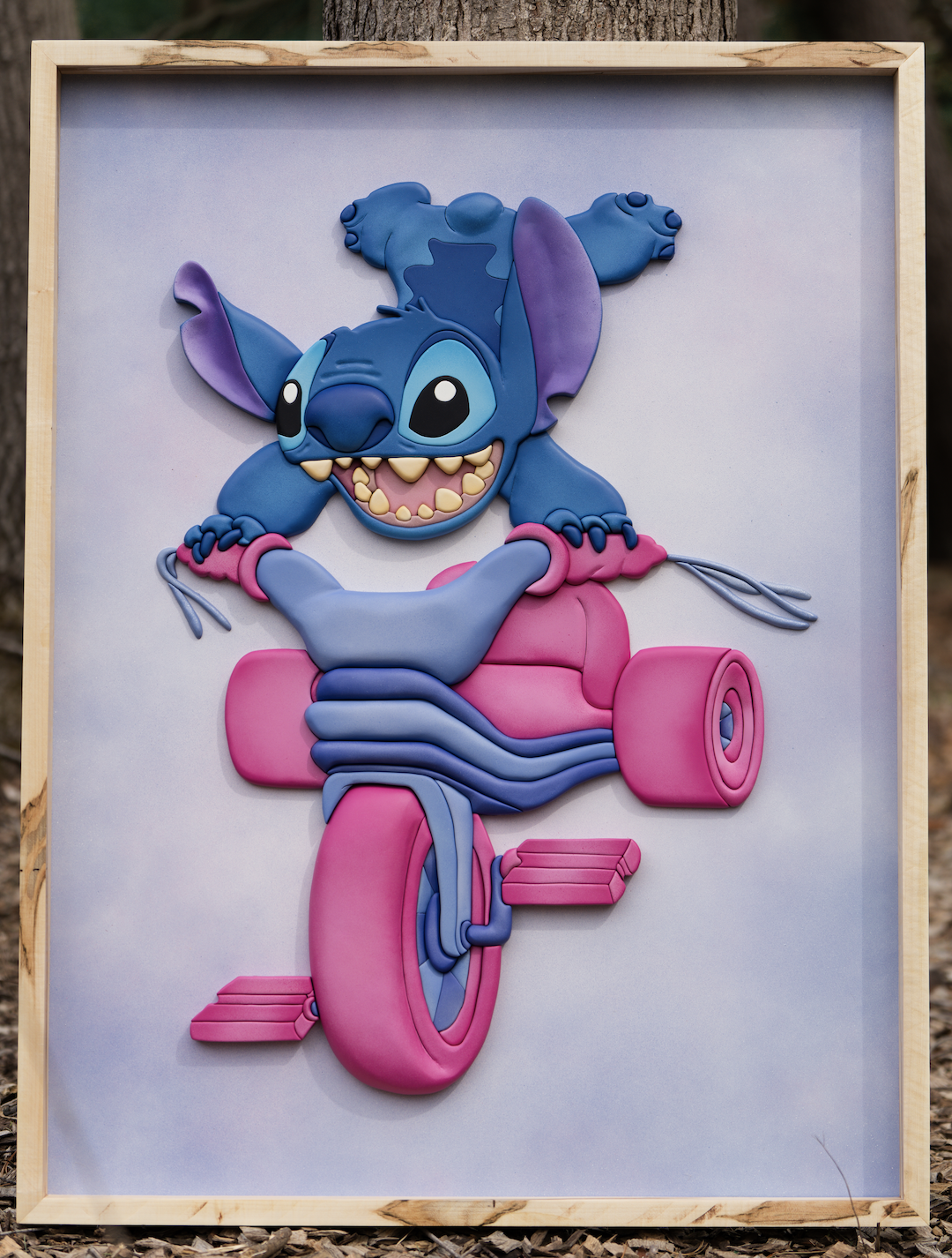 Colorful cartoon sculpture of Stitch from Lilo & Stitch riding a pink bike with a big grin, inside a wooden frame.