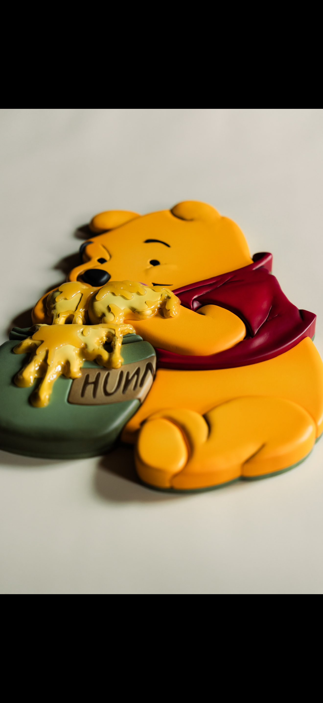 Cake decorated as Winnie the Pooh holding a honey pot labeled 'HUNNY' with honey dripping from it.