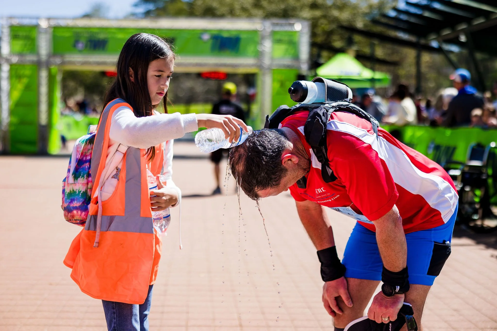 An orange-vested race volunteer cooling a runner with water after the finish