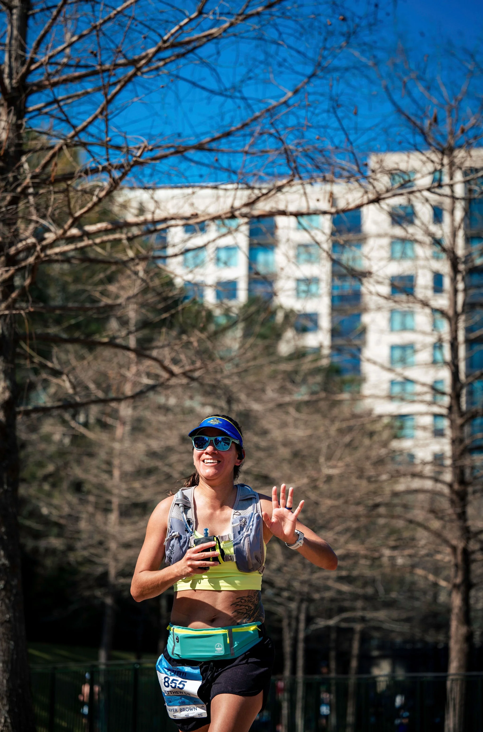 A runner smiling and waving along The Woodlands course