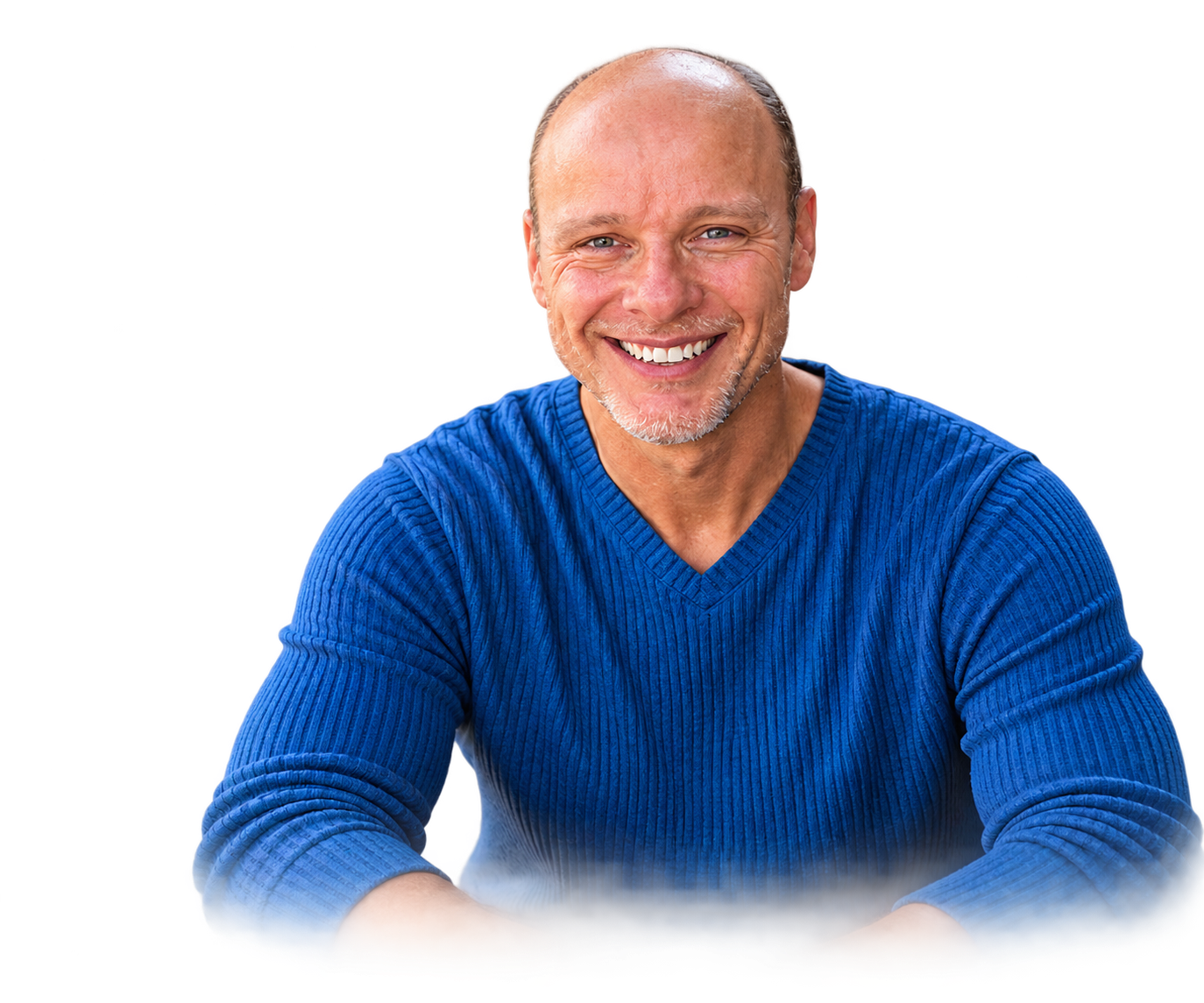 A smiling middle-aged man with a bald head and beard, wearing a blue ribbed sweater, sitting with his arms crossed in front of a background featuring red, white, and blue colors.