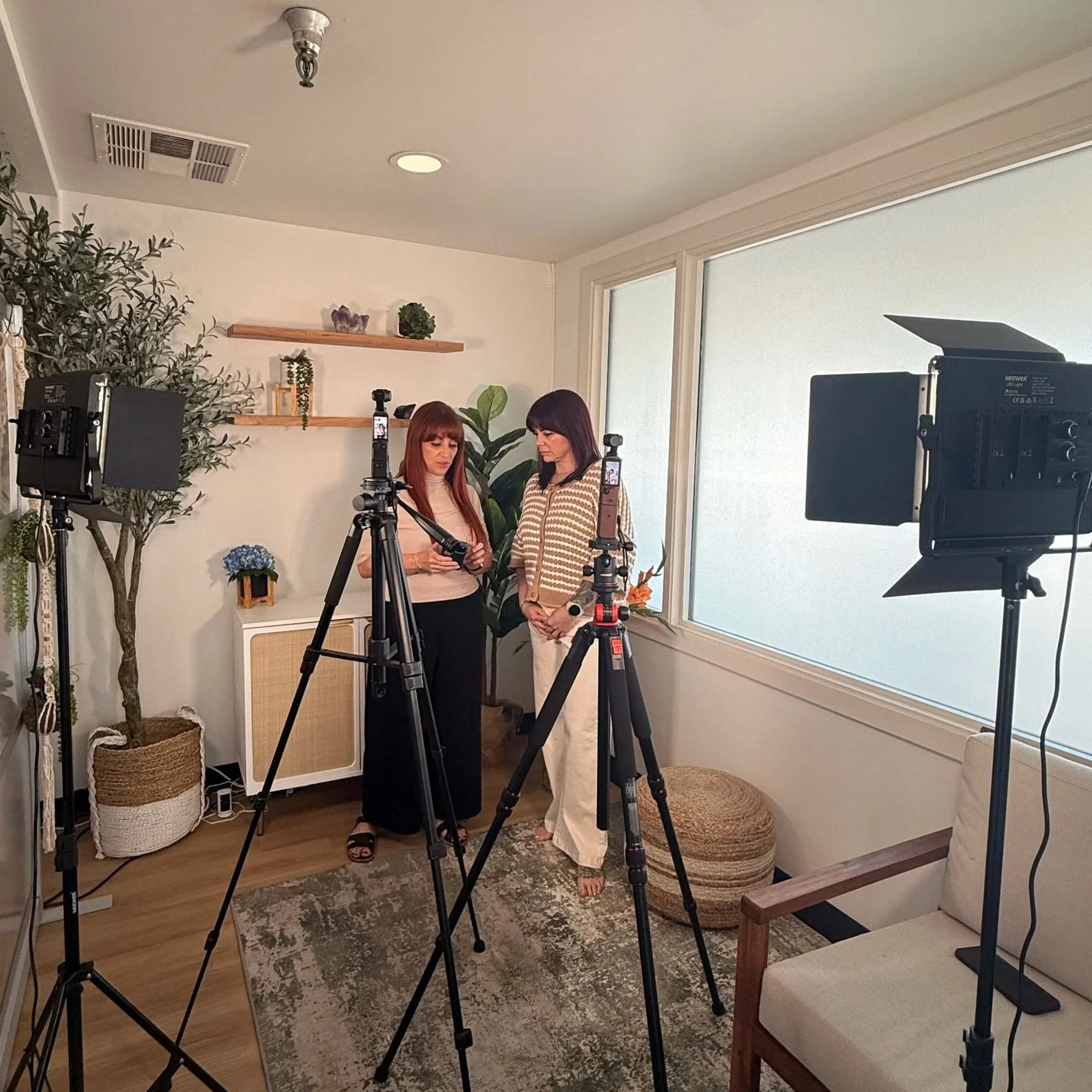 Two women filming social media content in a bright home studio with lights and tripods, behind the scenes with Poppy House Media