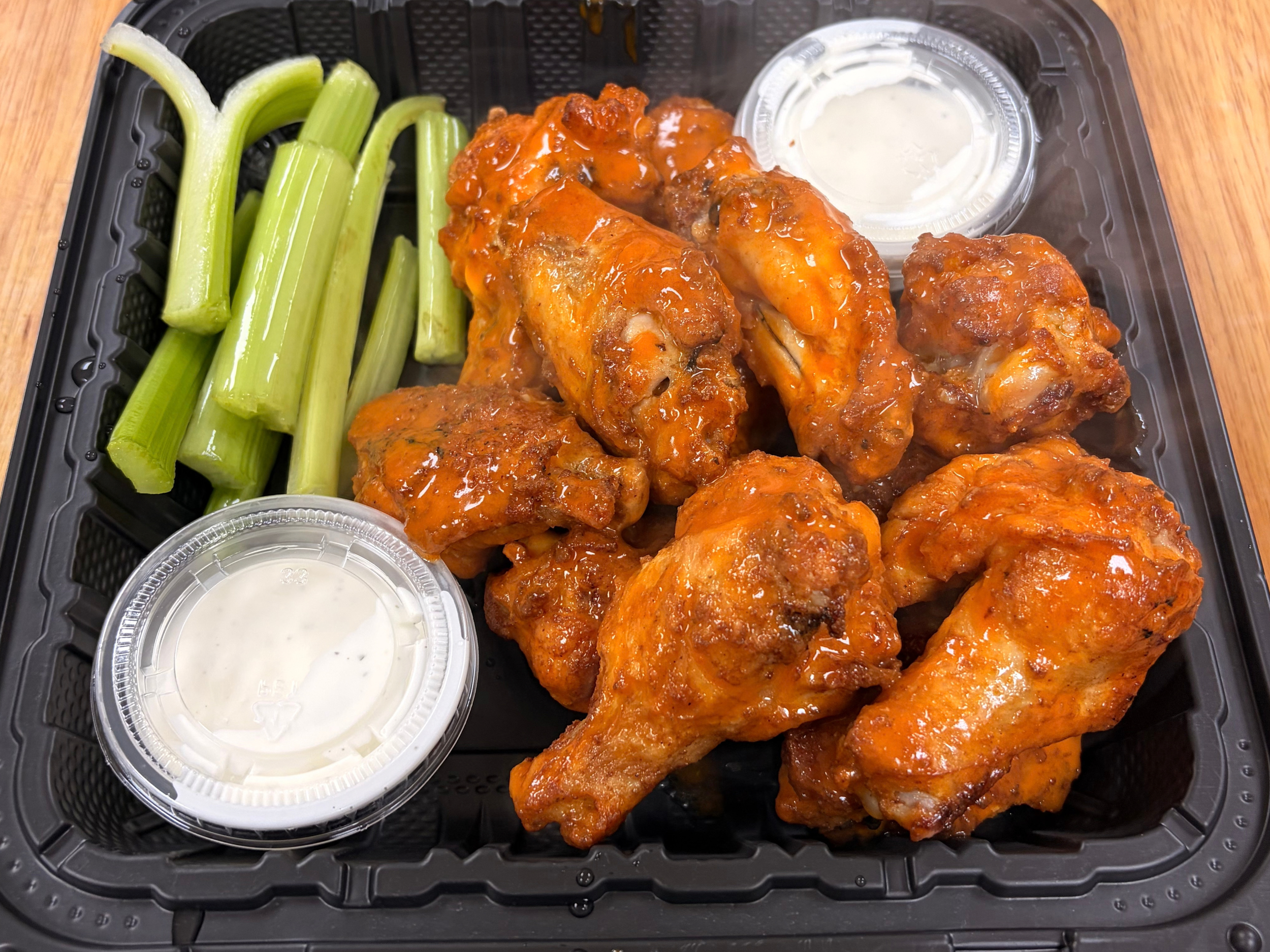 Takeout container with buffalo chicken wings, celery sticks, and dipping sauces.
