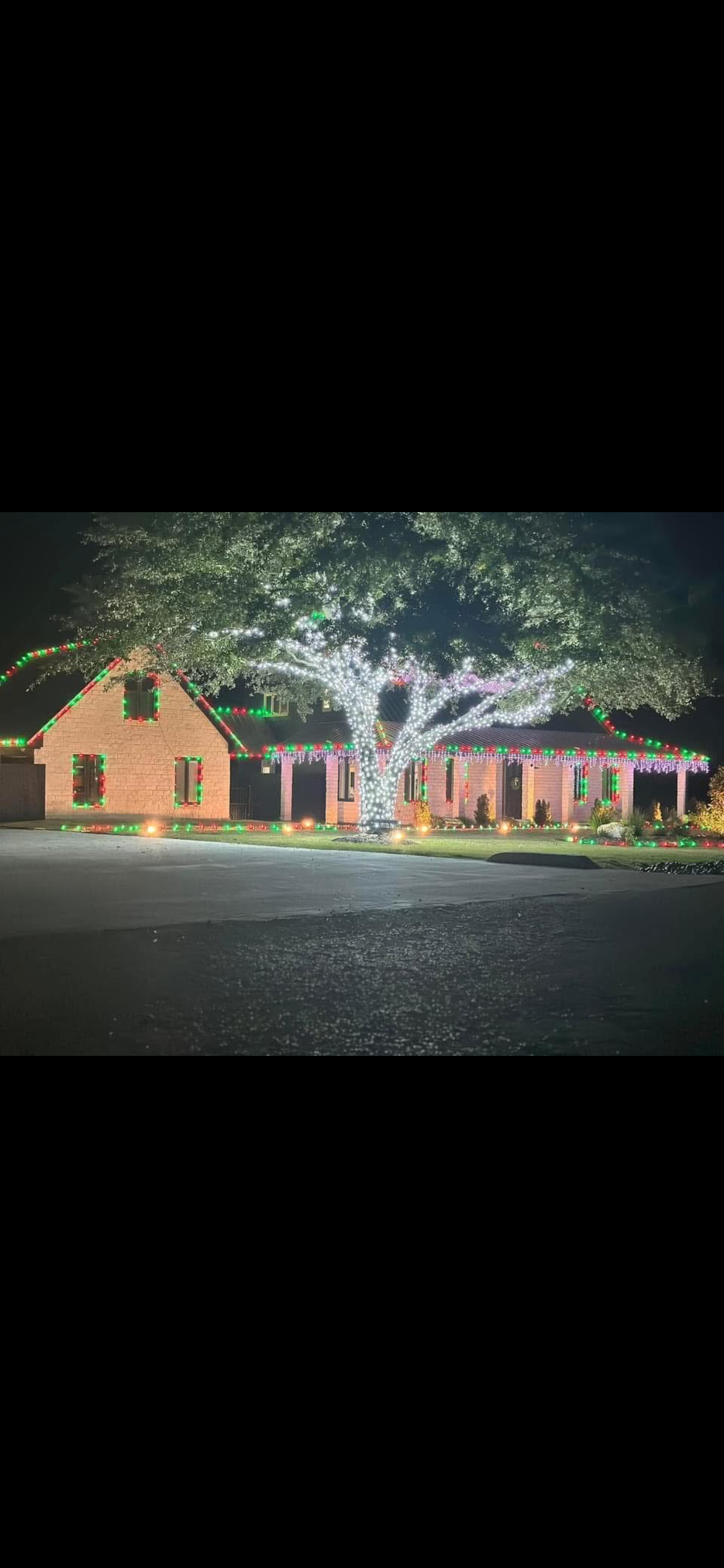 A house decorated with colorful Christmas lights and illuminated trees at night.