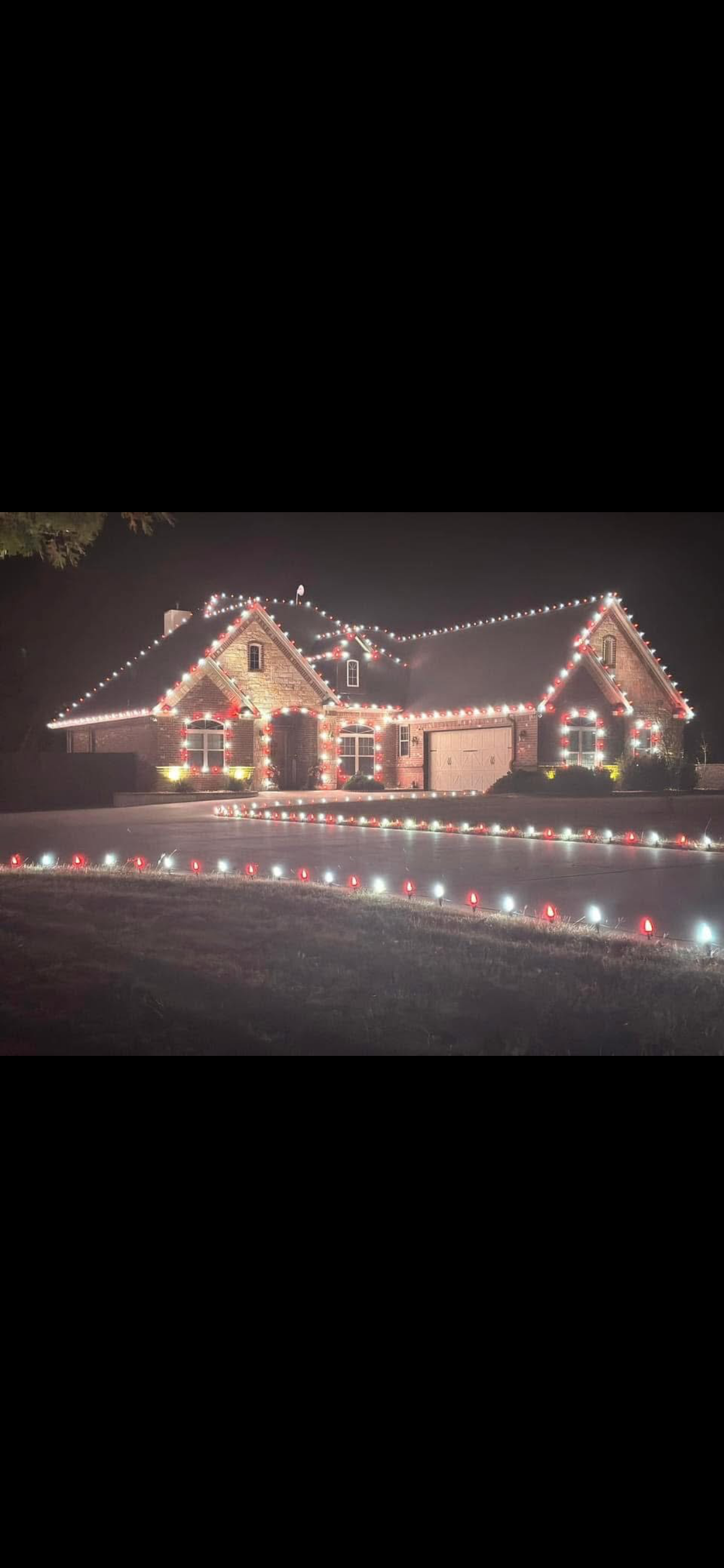 A house decorated with Christmas lights at night, including red and white lights outlining the roof, windows, and garage, with additional lights on the driveway and lawn.