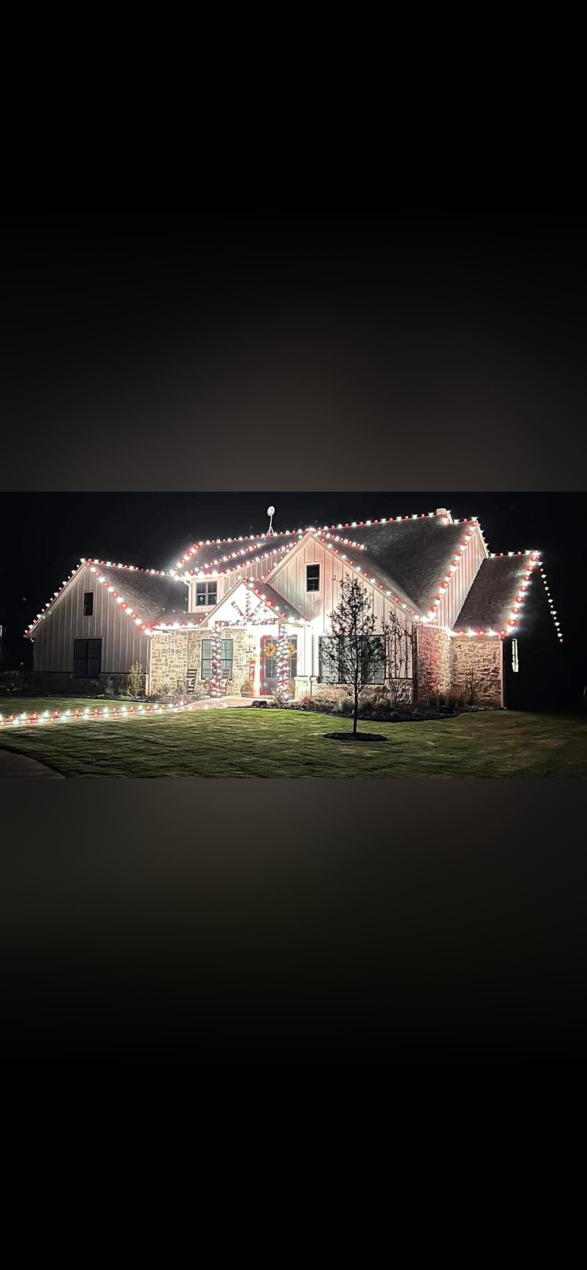 A house decorated with Christmas lights at night, with a well-maintained lawn and a small tree in the front yard.
