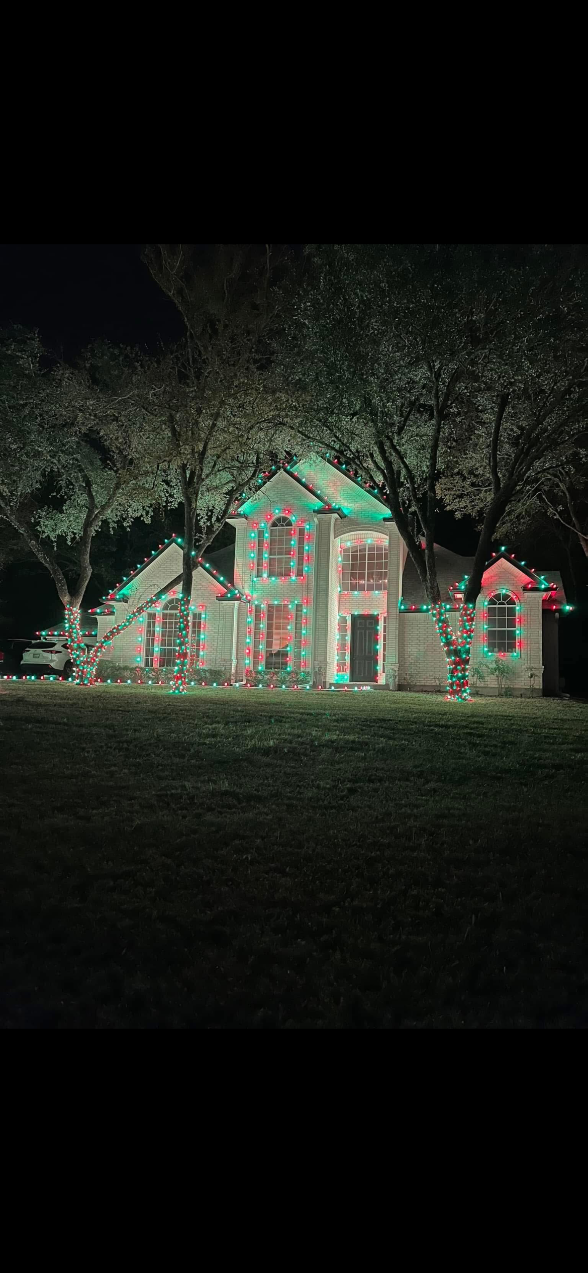 A house decorated with red and green Christmas lights at night, with trees also wrapped in lights.