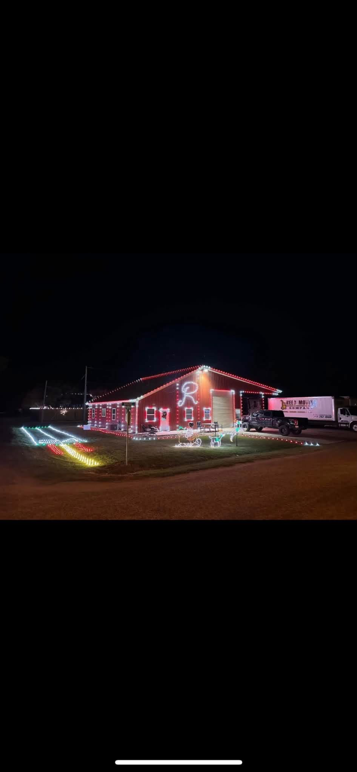 House decorated with Christmas lights, including reindeer and candy canes outside, with a truck parked beside it at night.