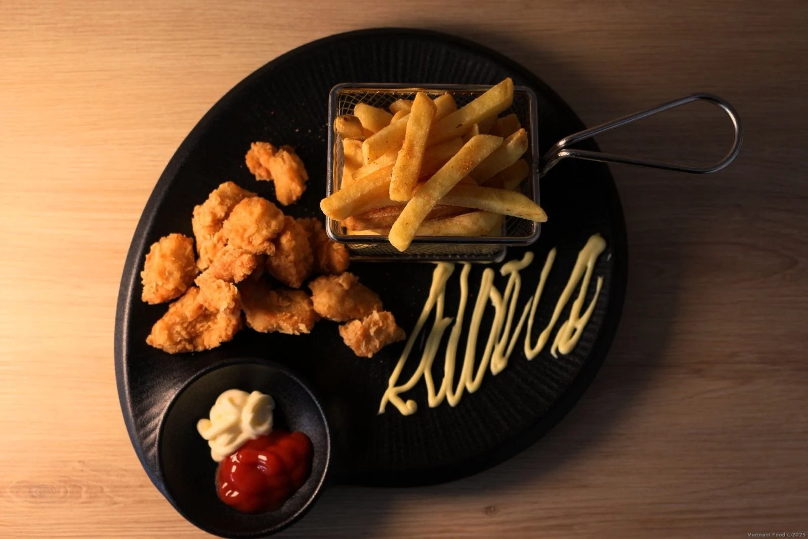 Fried chicken strips with French fries in a small basket, ketchup and mayonnaise on a black plate with the word 'RUMINOS' written in mayonnaise.