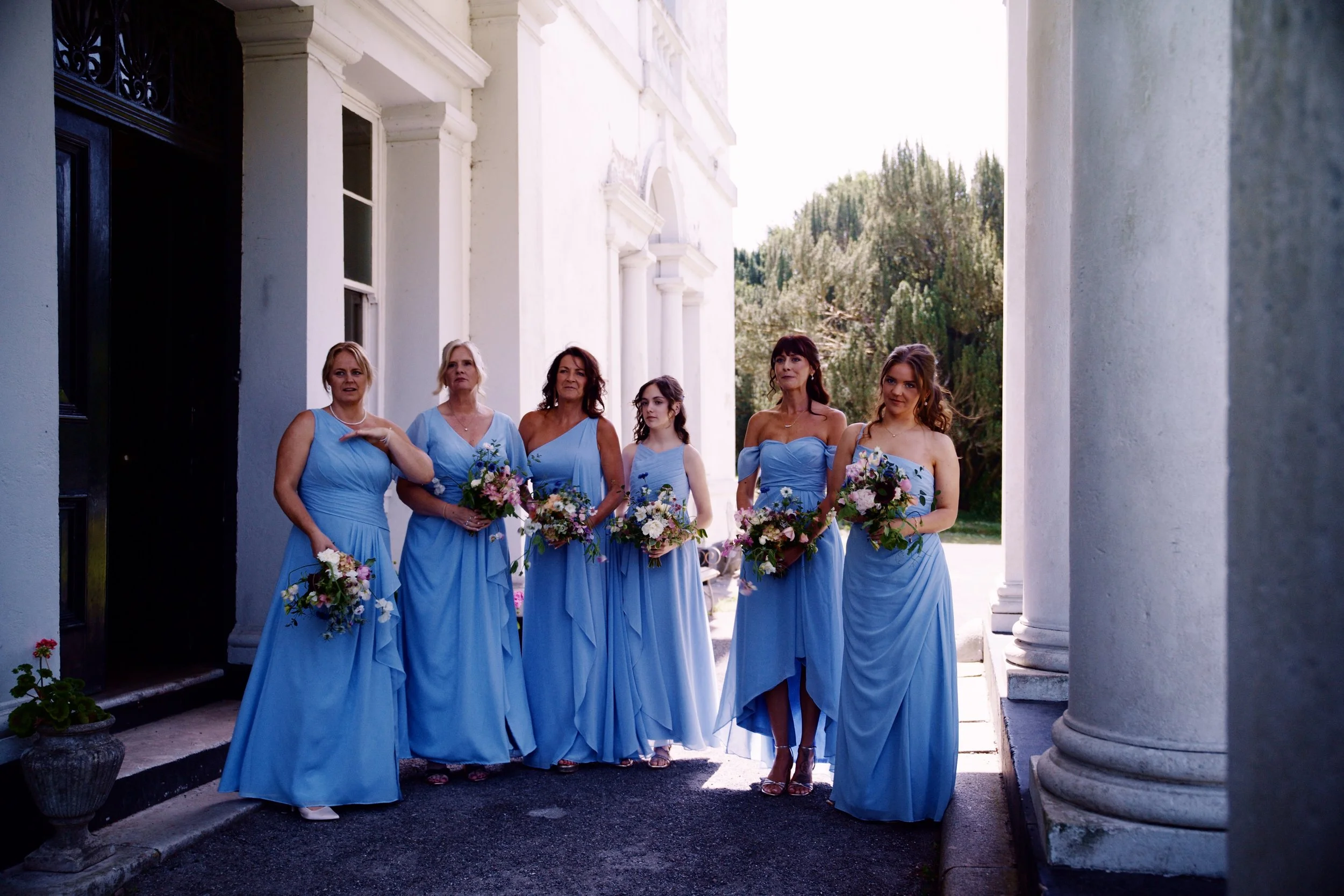 Six bridesmaids all in floor length blue gowns holding flower bouquets