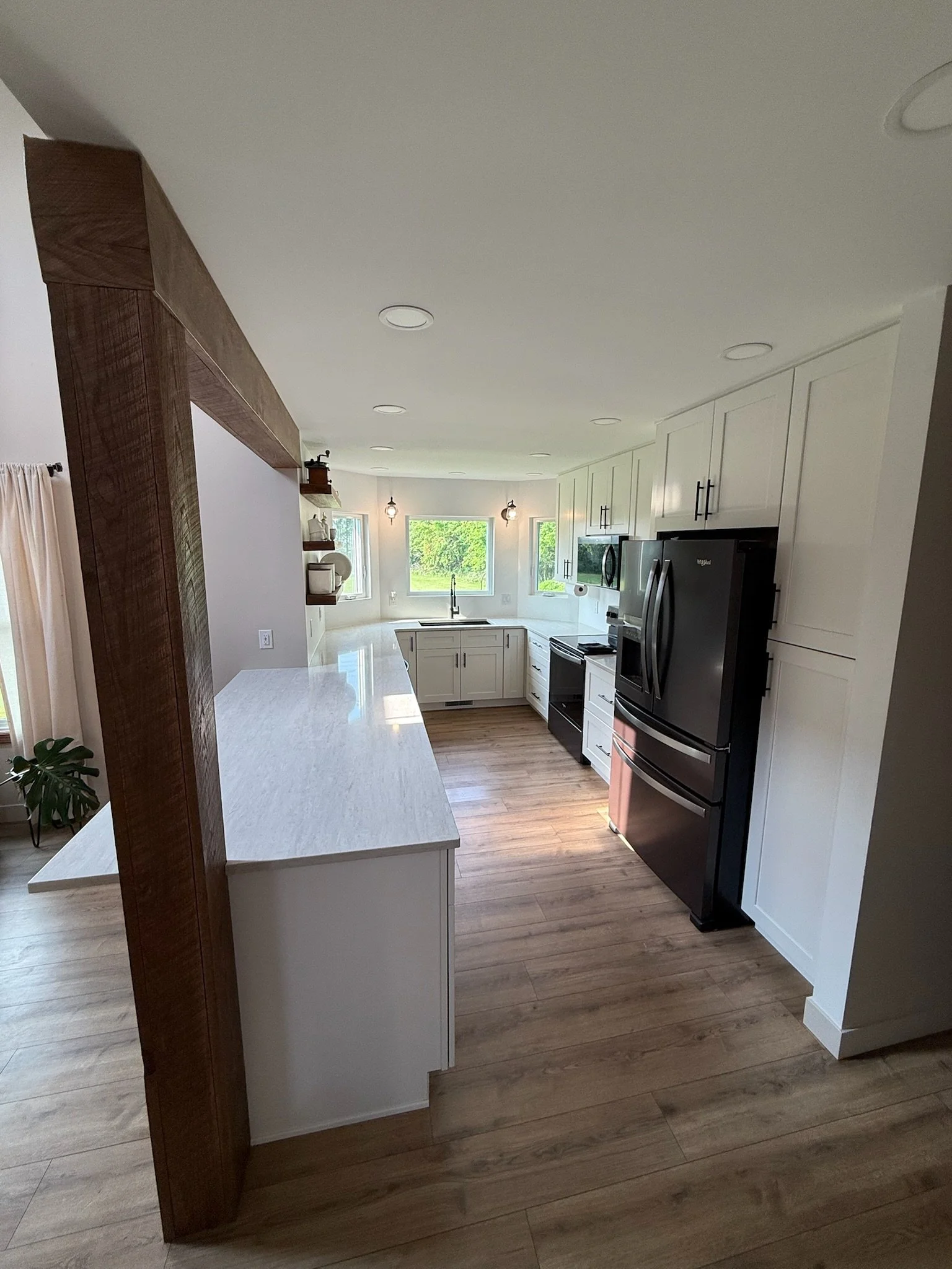 A modern kitchen with white cabinets, stainless steel appliances, a black refrigerator, hardwood flooring, and a white marble island counter.