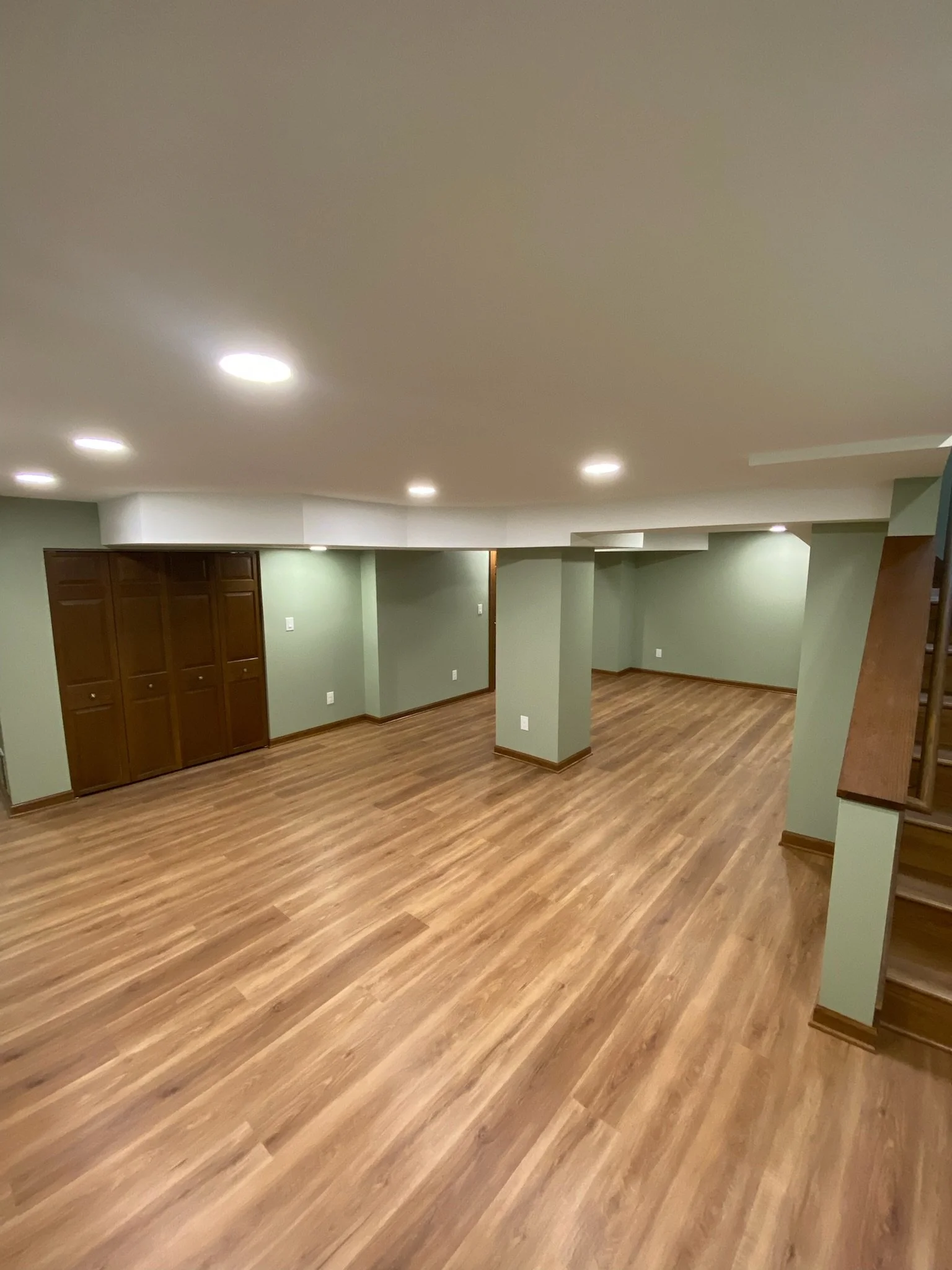 Basement with wood flooring, green walls, and a ceiling with recessed lighting.