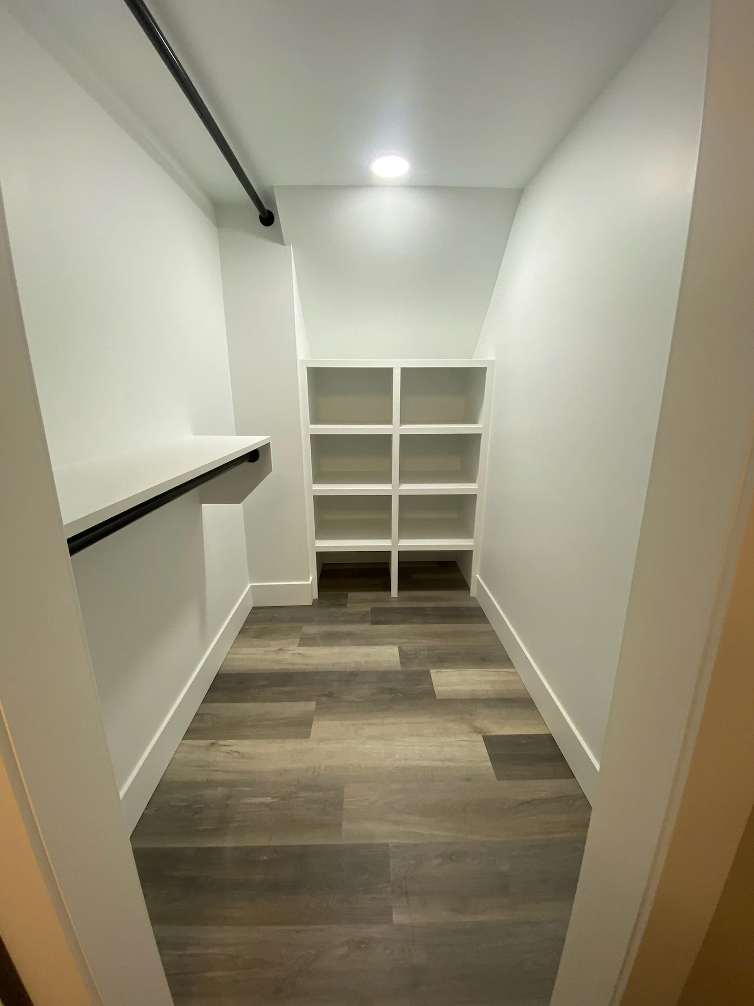 Empty walk-in closet with white shelves, black clothing rods, and wooden flooring.