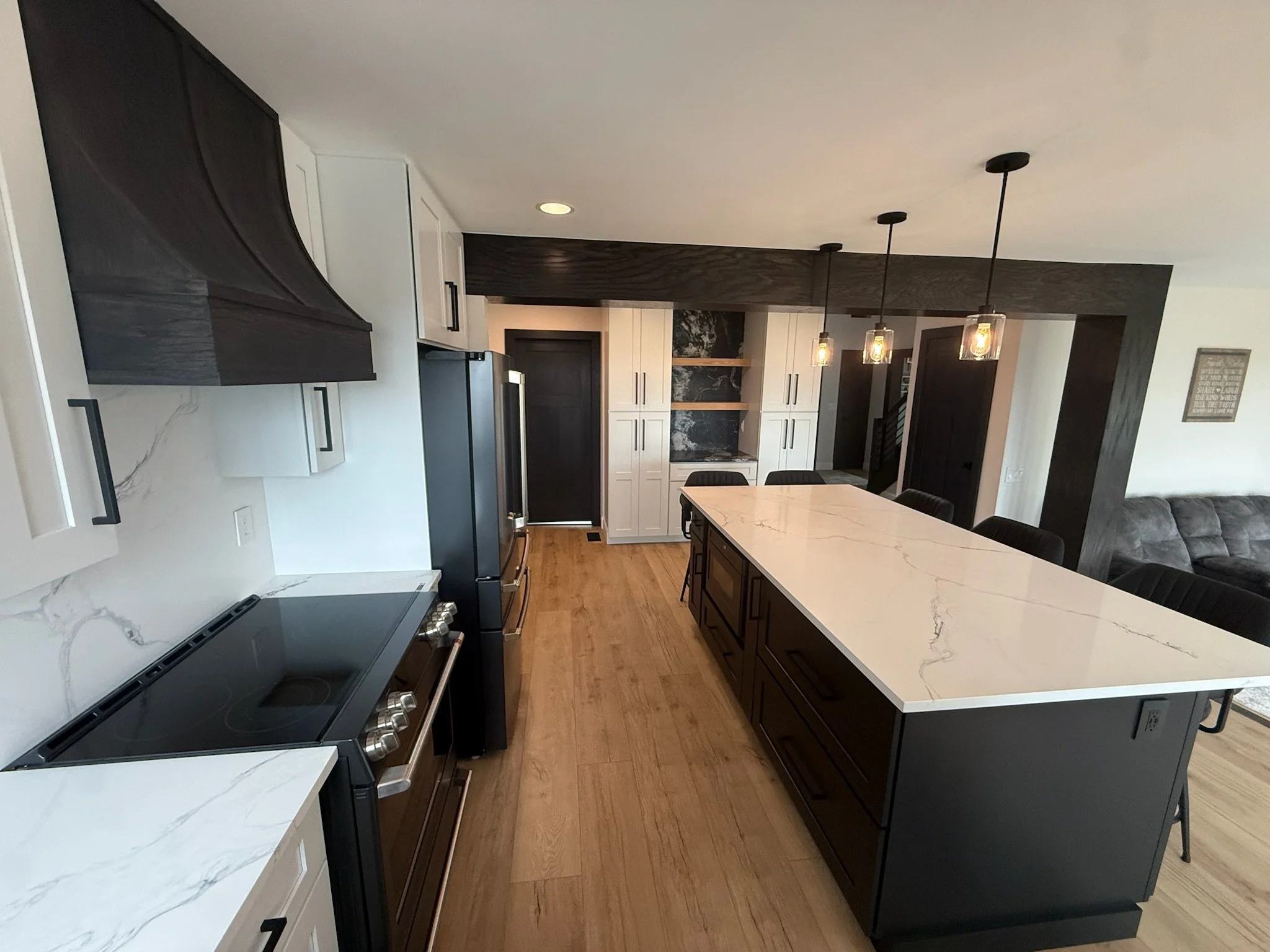 Modern kitchen with black and white cabinets, marble countertops, and pendant lights over a large kitchen island.
