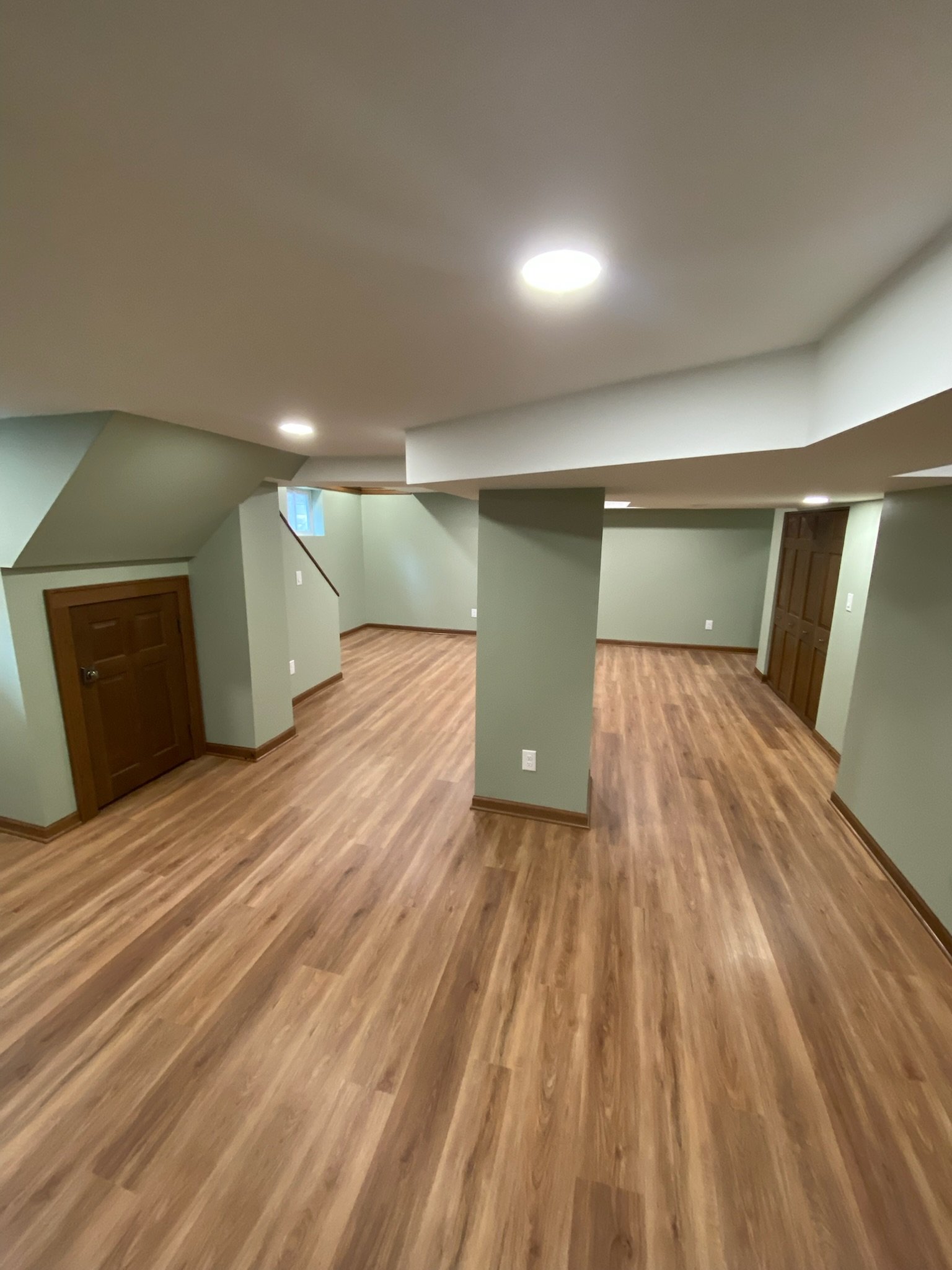 Empty basement with wood flooring, green walls, and a ceiling with recessed lighting.
