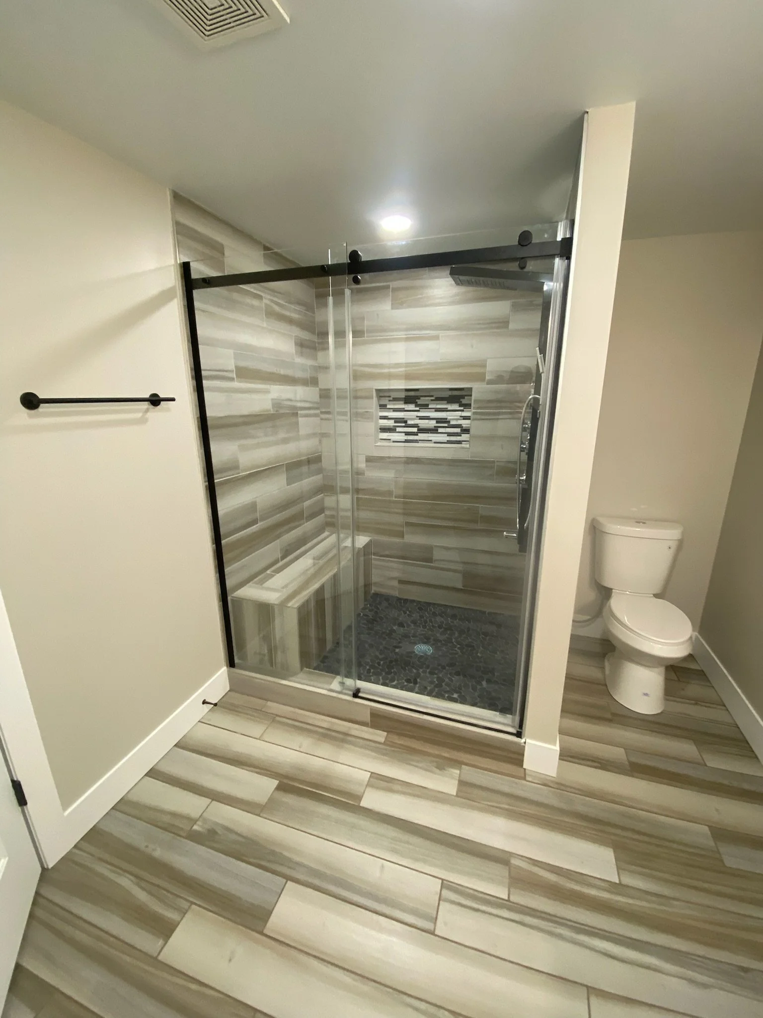 Bathroom with a glass shower enclosure, tiled shower wall with a built-in niche, and a toilet on the right.