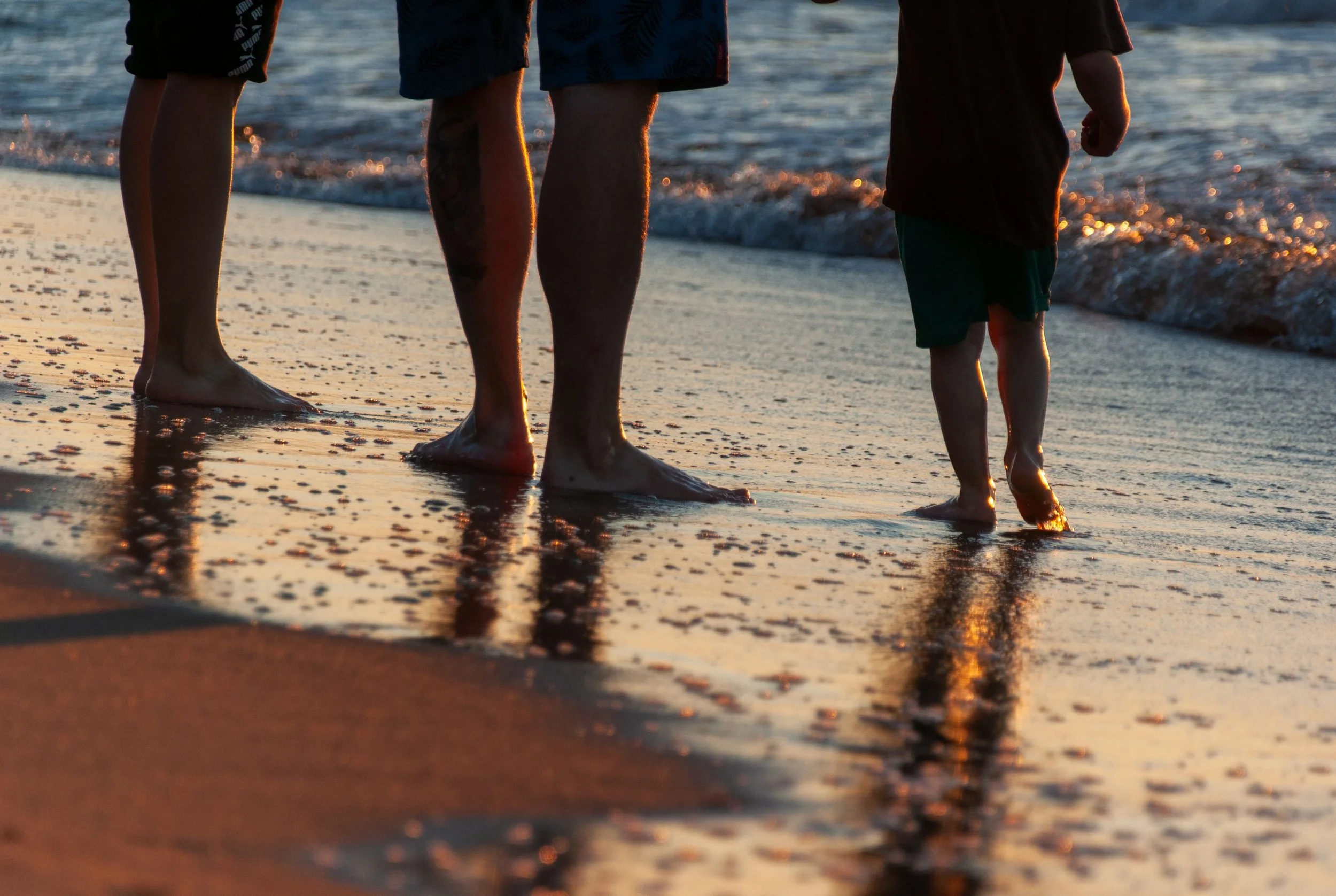 People walking along the beach at sunset with their feet in the shallow water.