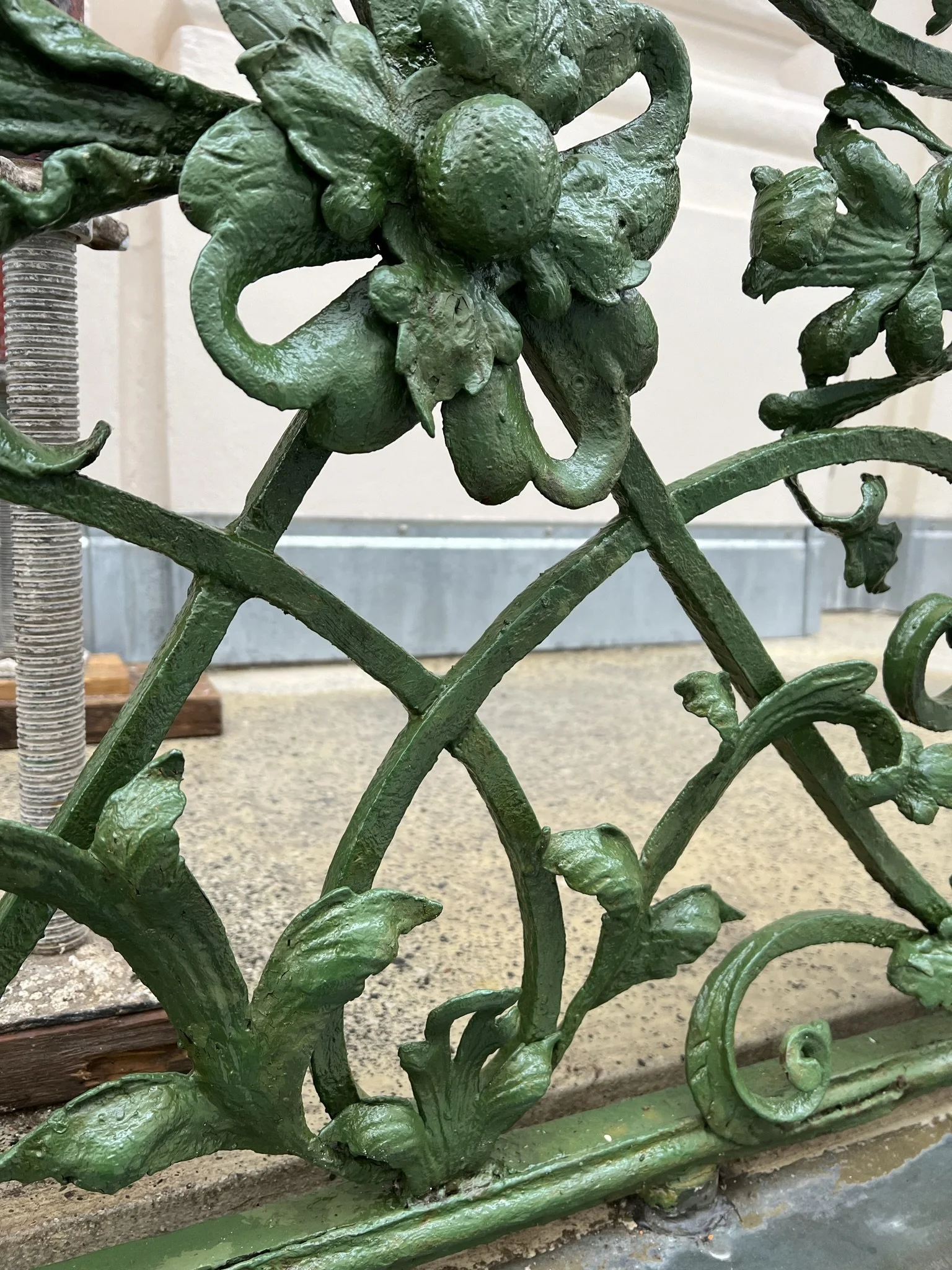Nahaufnahme eines kunstvollen, grünen, metallischen Zauns mit Blatt- und Fruchtmotiven.