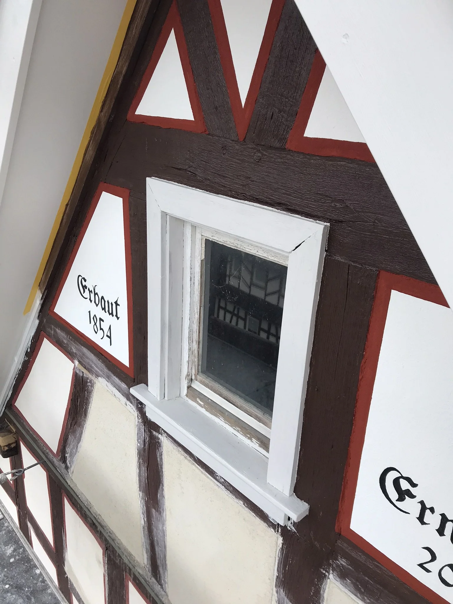 Ein Holzrahmen mit einem kleinen Fenster und einer Tafel, die auf Deutsch steht, mit roten und weißen Elementen.