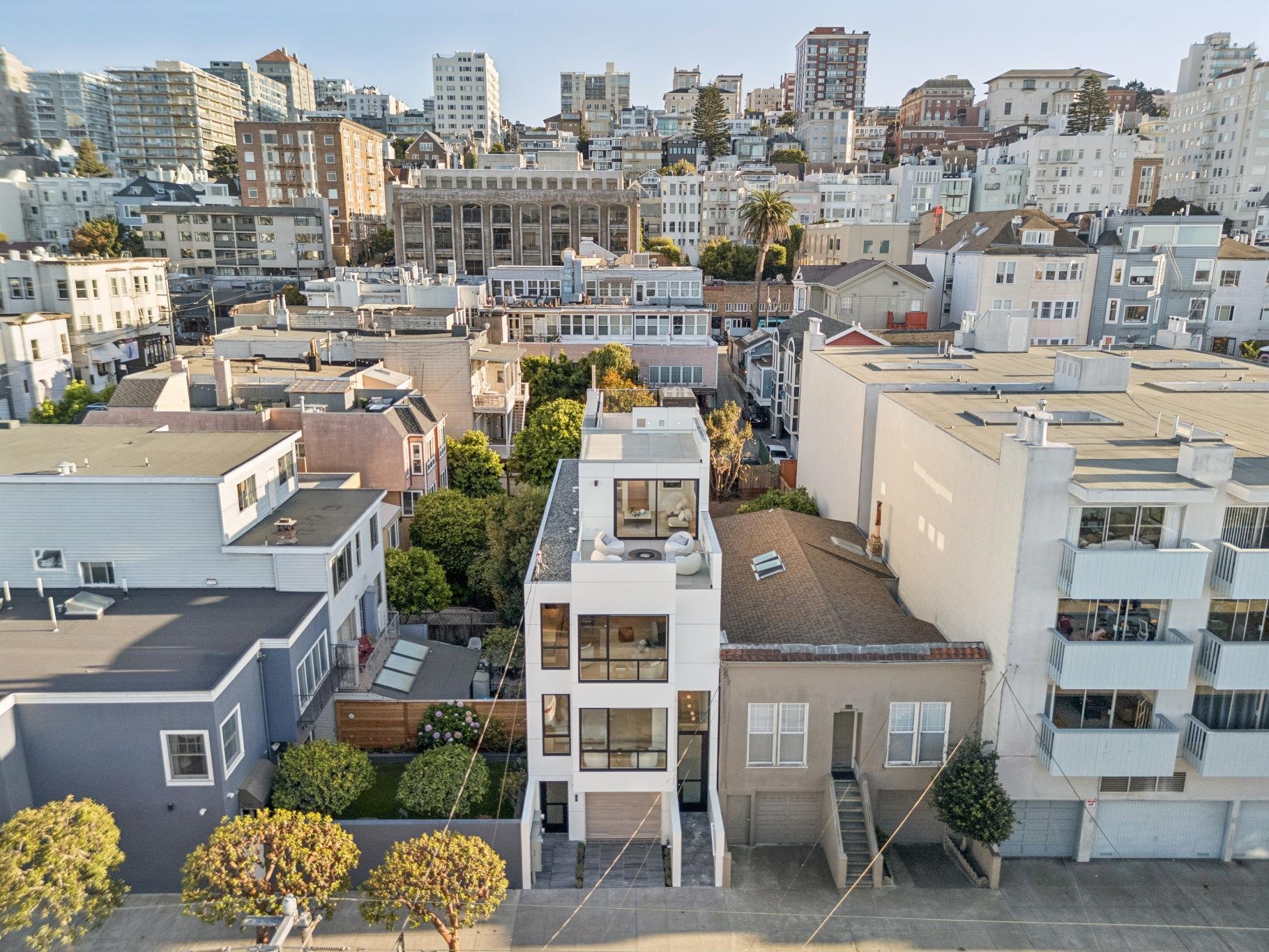 Aerial view of a city neighborhood showing a mix of modern and older buildings with a rooftop patio and lush trees.