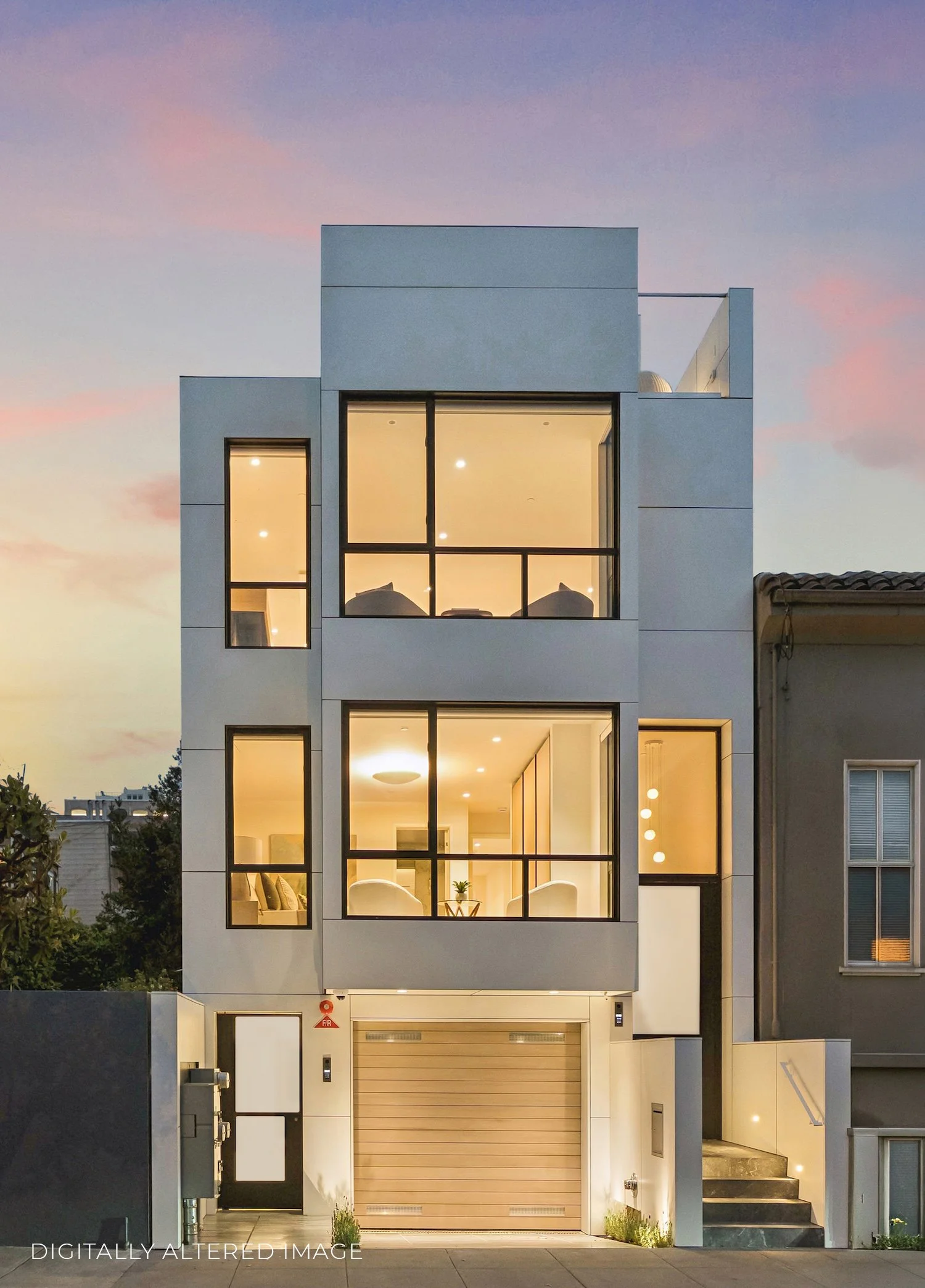 Modern multi-story house with large glass windows, a garage with a beige door, and external lighting, set against a sunset sky.
