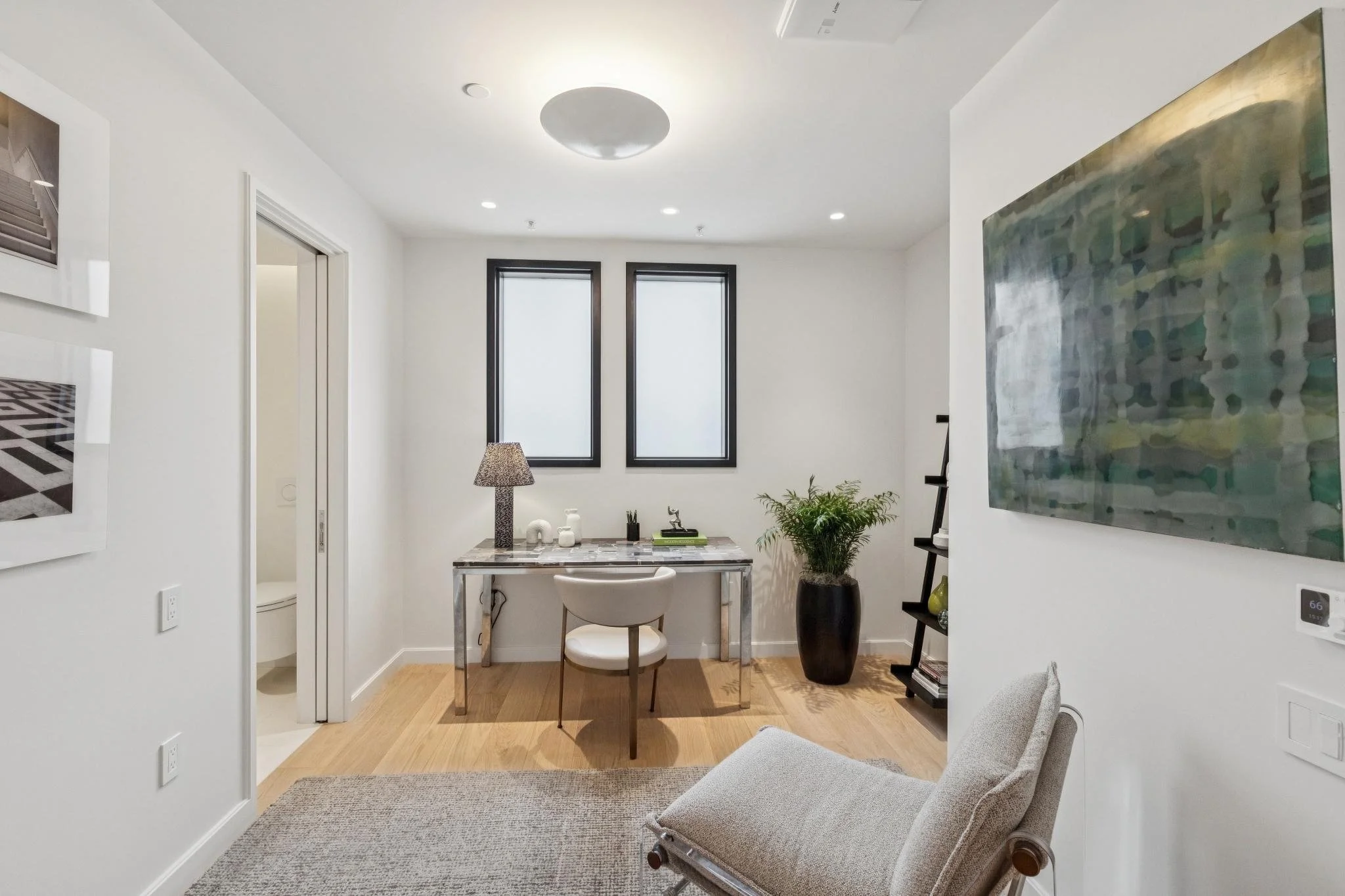 Modern living room with artwork, a small table, a chair, and large windows.