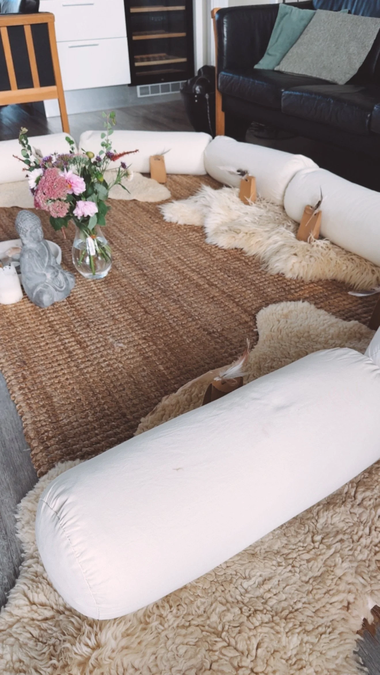 Ein Raum mit einem weißen, aufblasbaren Gegenstand, der auf einem weichen, kuscheligen Teppich liegt. Im Hintergrund sind Sofas, eine Vase mit Blumen und einige Dekorationsgegenstände sichtbar.