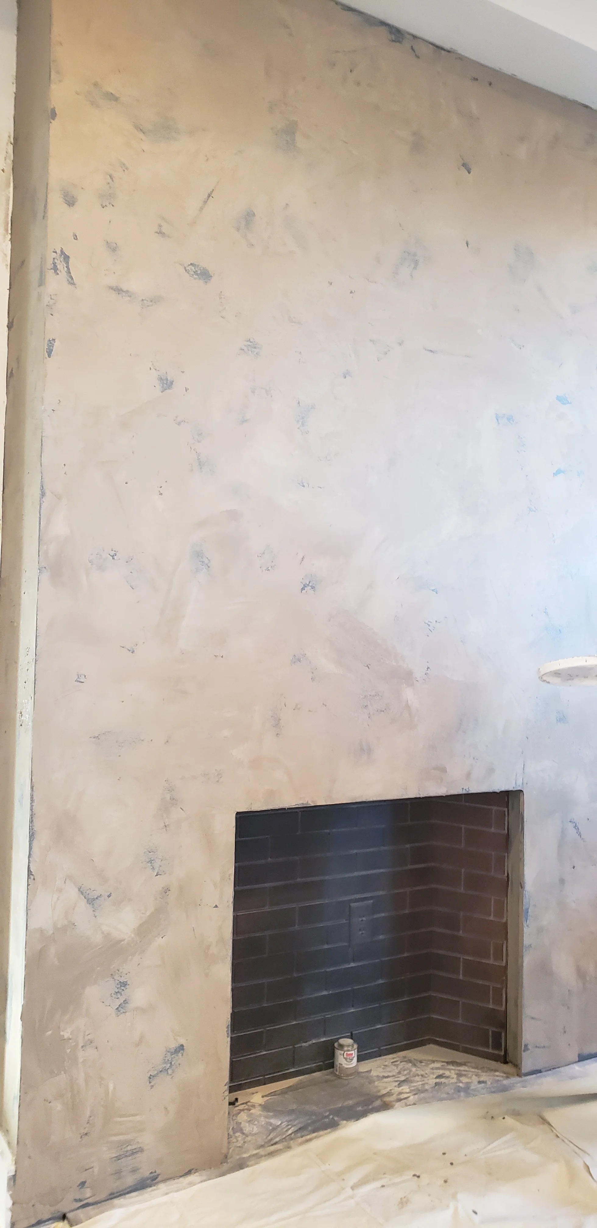 Fireplace during an earlier stage of the Venetian plaster finish, with floor protection and tools nearby.