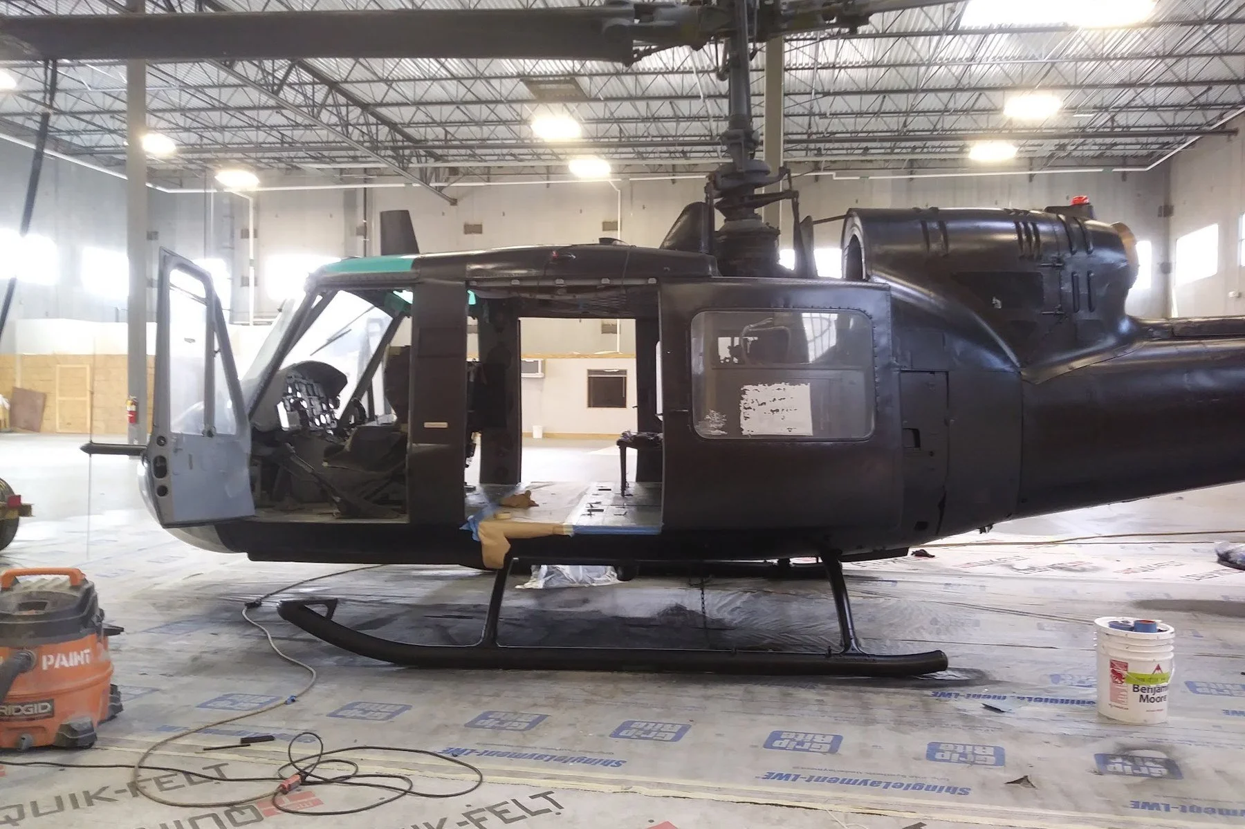 Full-size helicopter sprayed black inside a studio warehouse for a film shot, with the floor masked off during the job