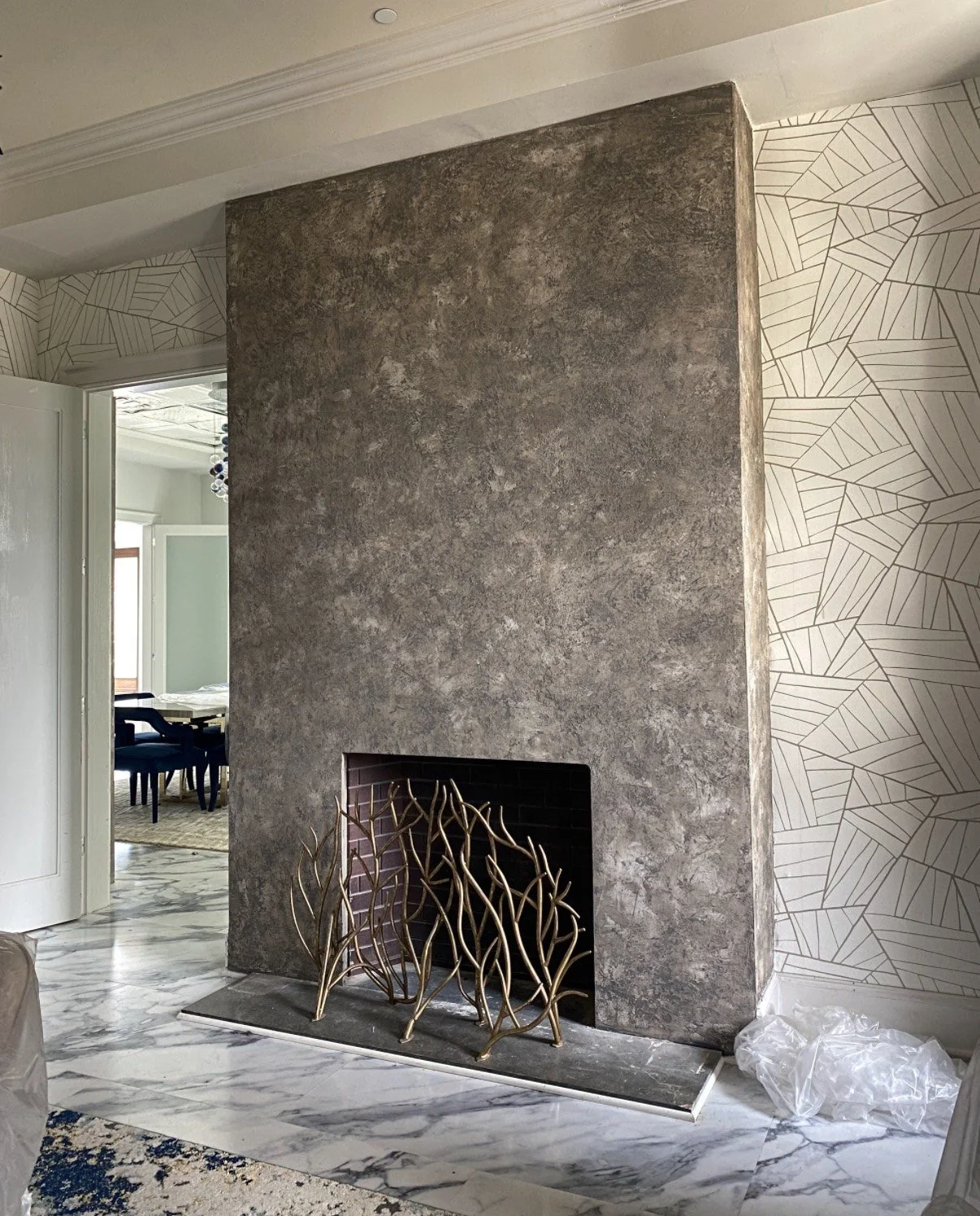 Floor-to-ceiling fireplace surround in burnished Venetian plaster, mottled dark and light gray, between geometric wallpaper and a marble floor in a private home